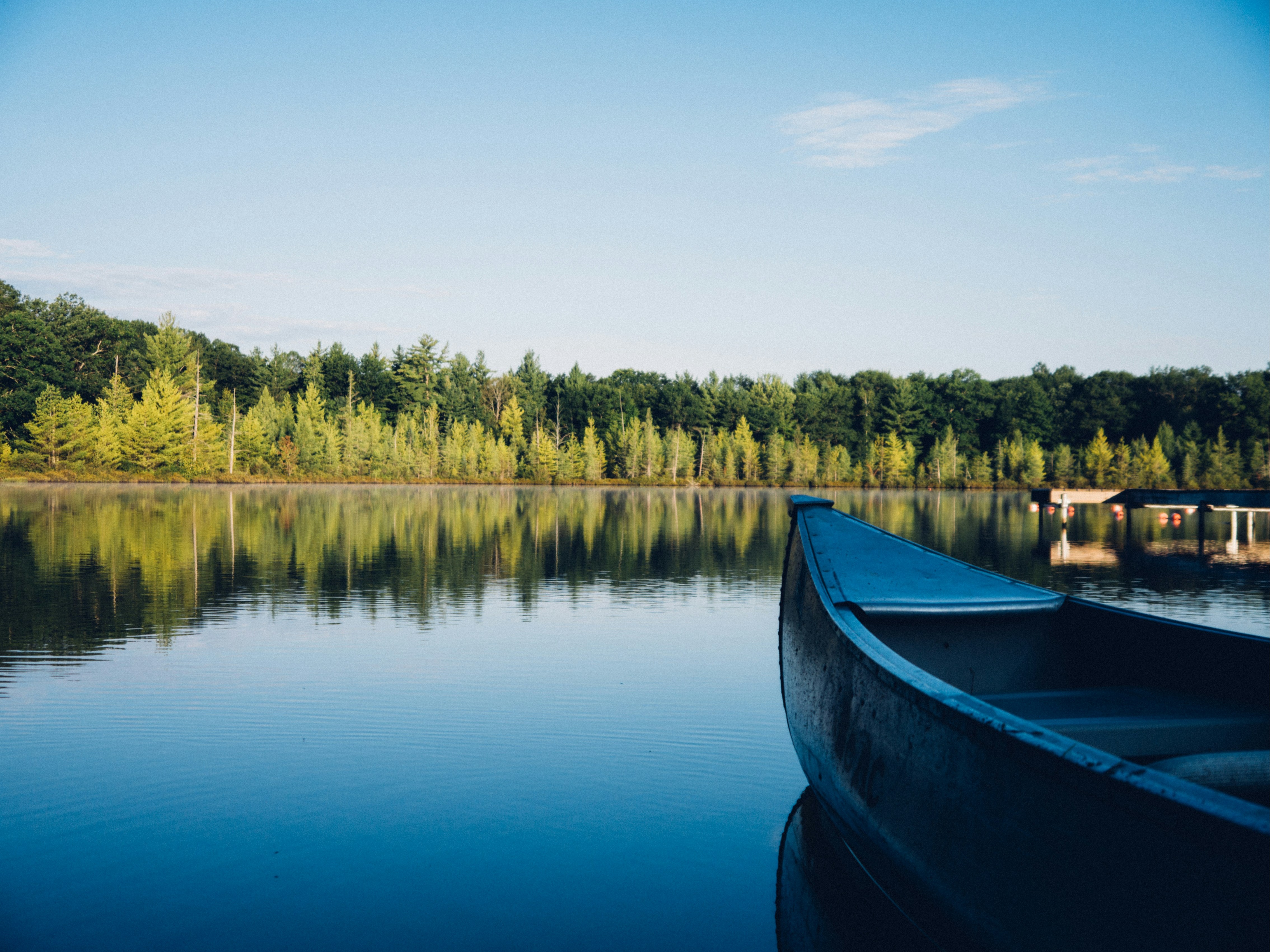 The image features the bow of a blue canoe on calm waters, reflecting the surrounding trees and clear sky.