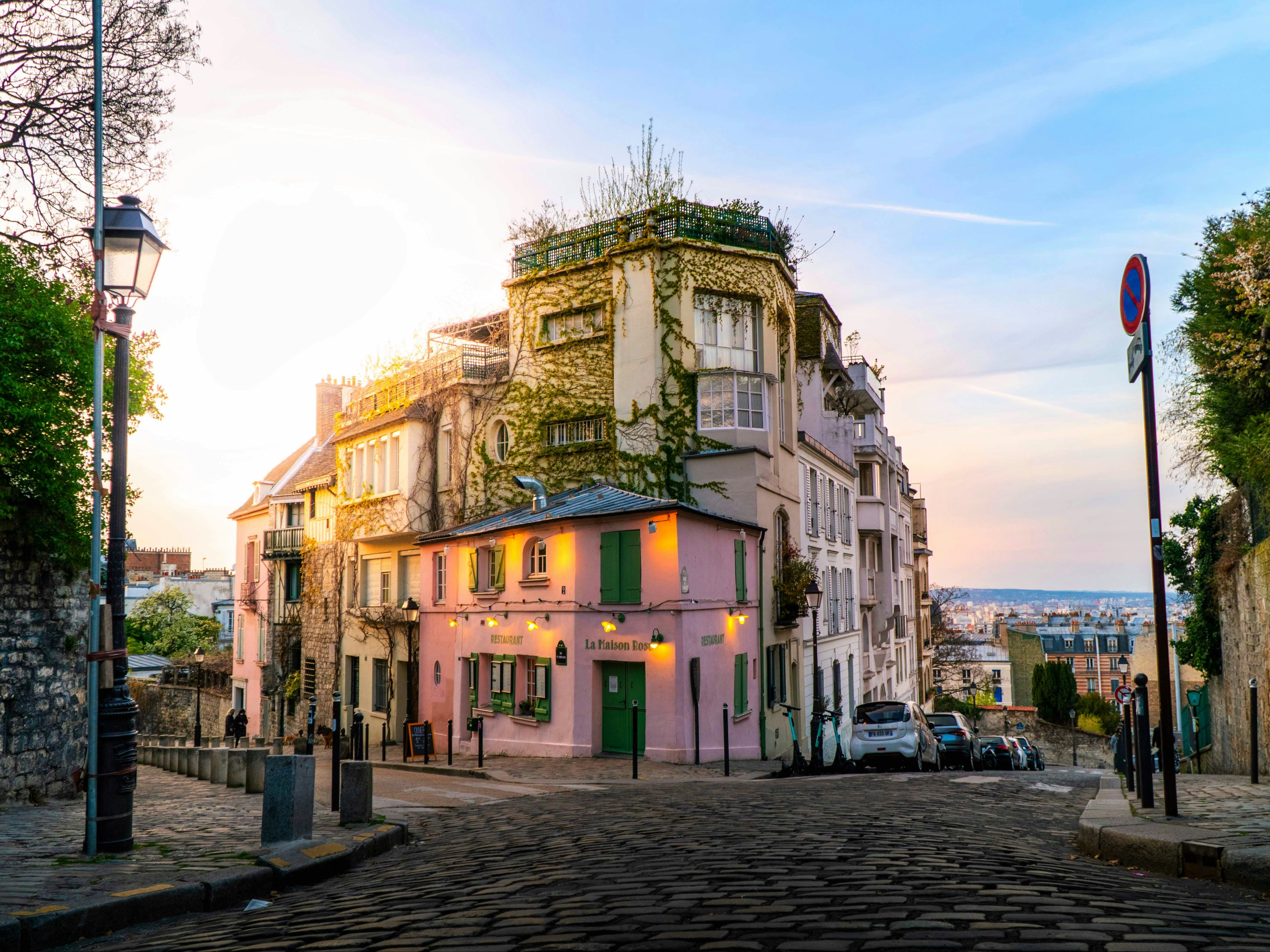 The image showcases a picturesque street corner in Montmartre, Paris, adorned with lush greenery and bathed in the warm glow of a sunset.