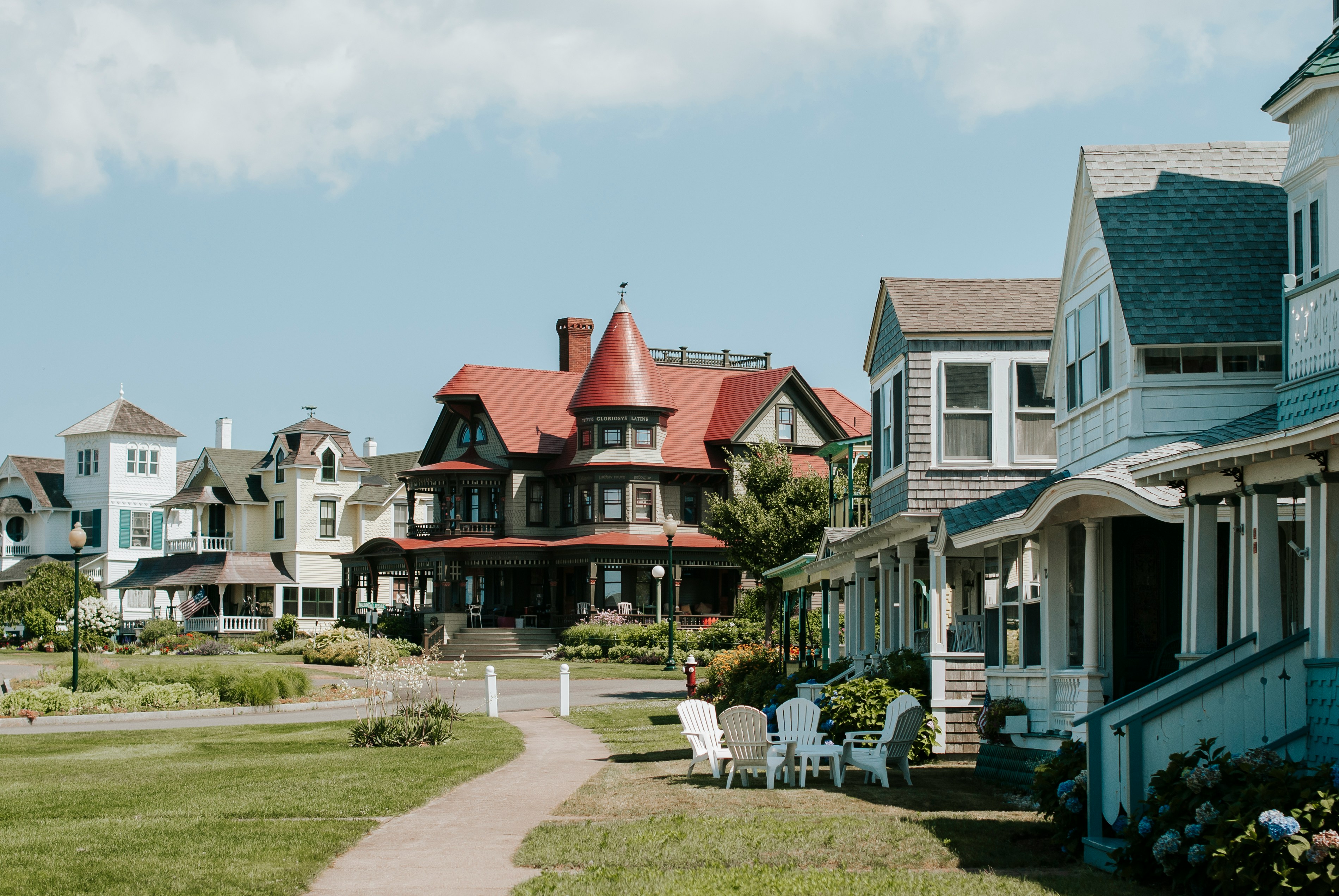 A scene of a path with different styles of houses with lawns and white chairs outside.