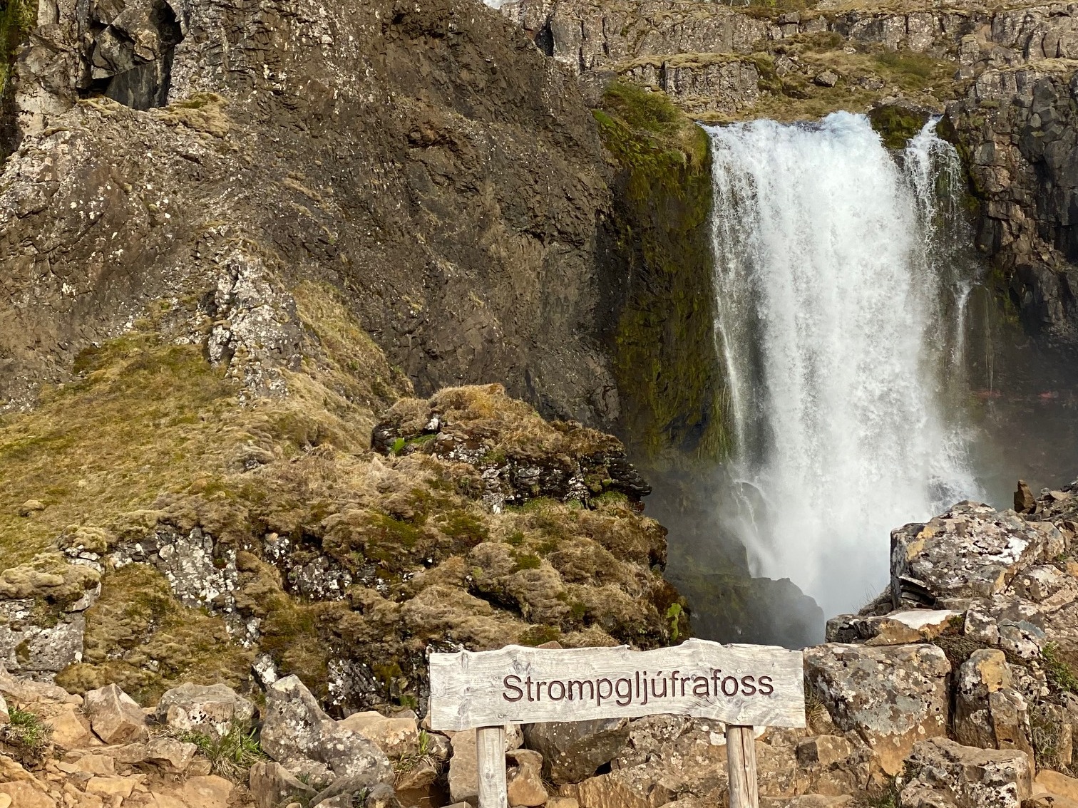 Waterfall from a mountain with a hiking path on a sunny day.