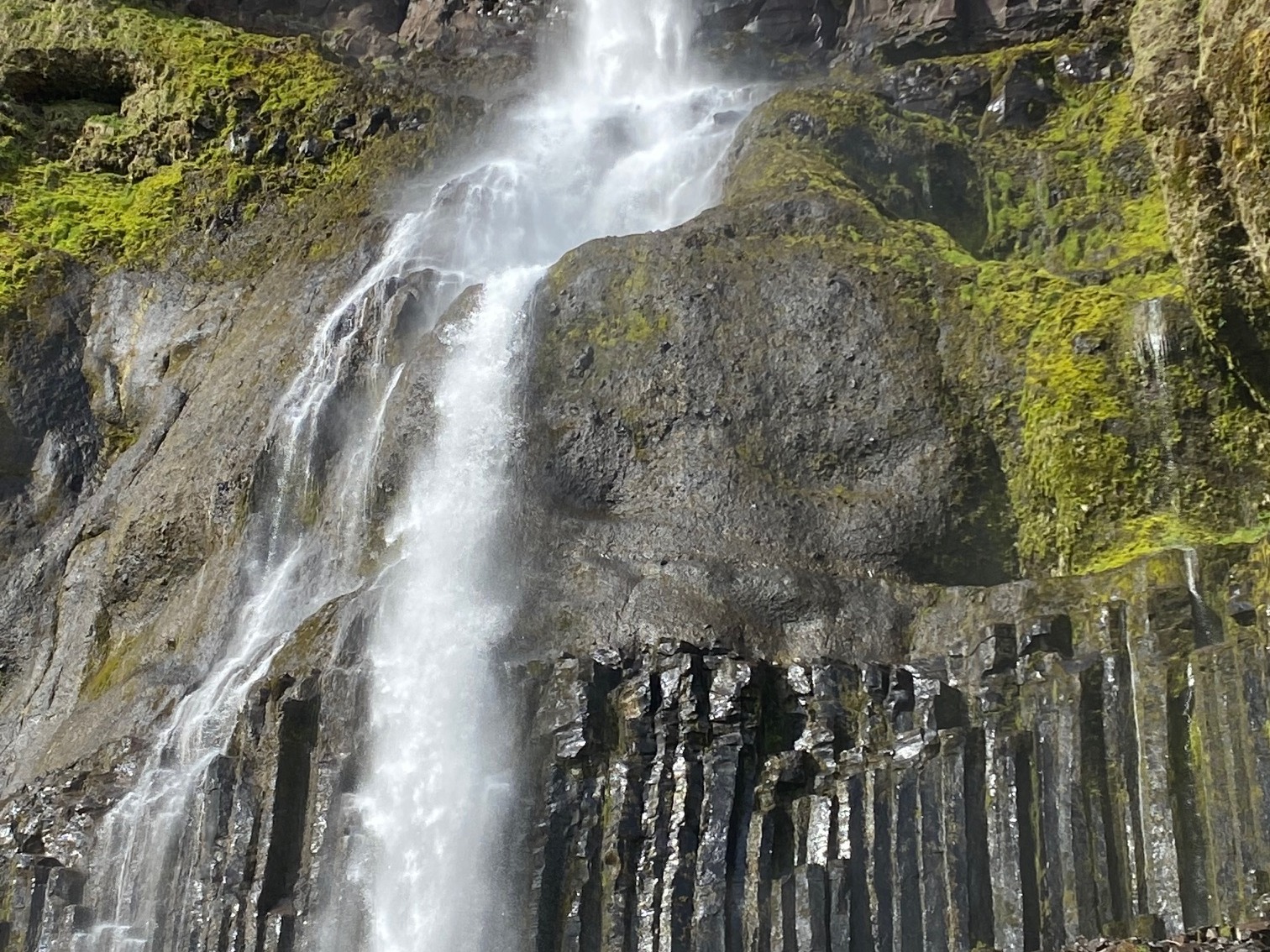Waterfall from a high mountain on a sunny day surrounded by greenery.
