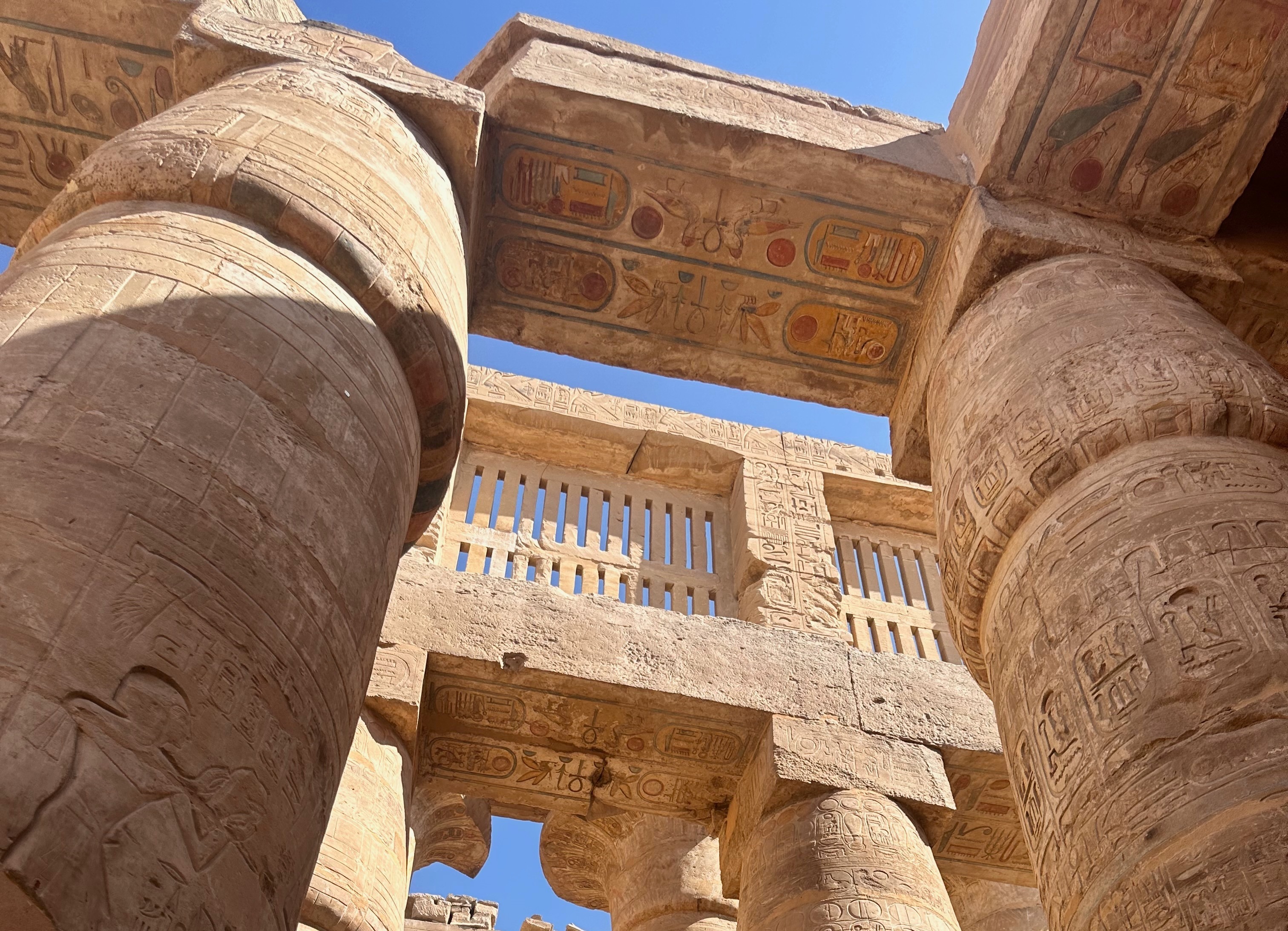 The image captures a close-up view of ancient Egyptian hieroglyphs on towering columns set against a vivid blue sky, showcasing the magnificence and detail of historical architecture.