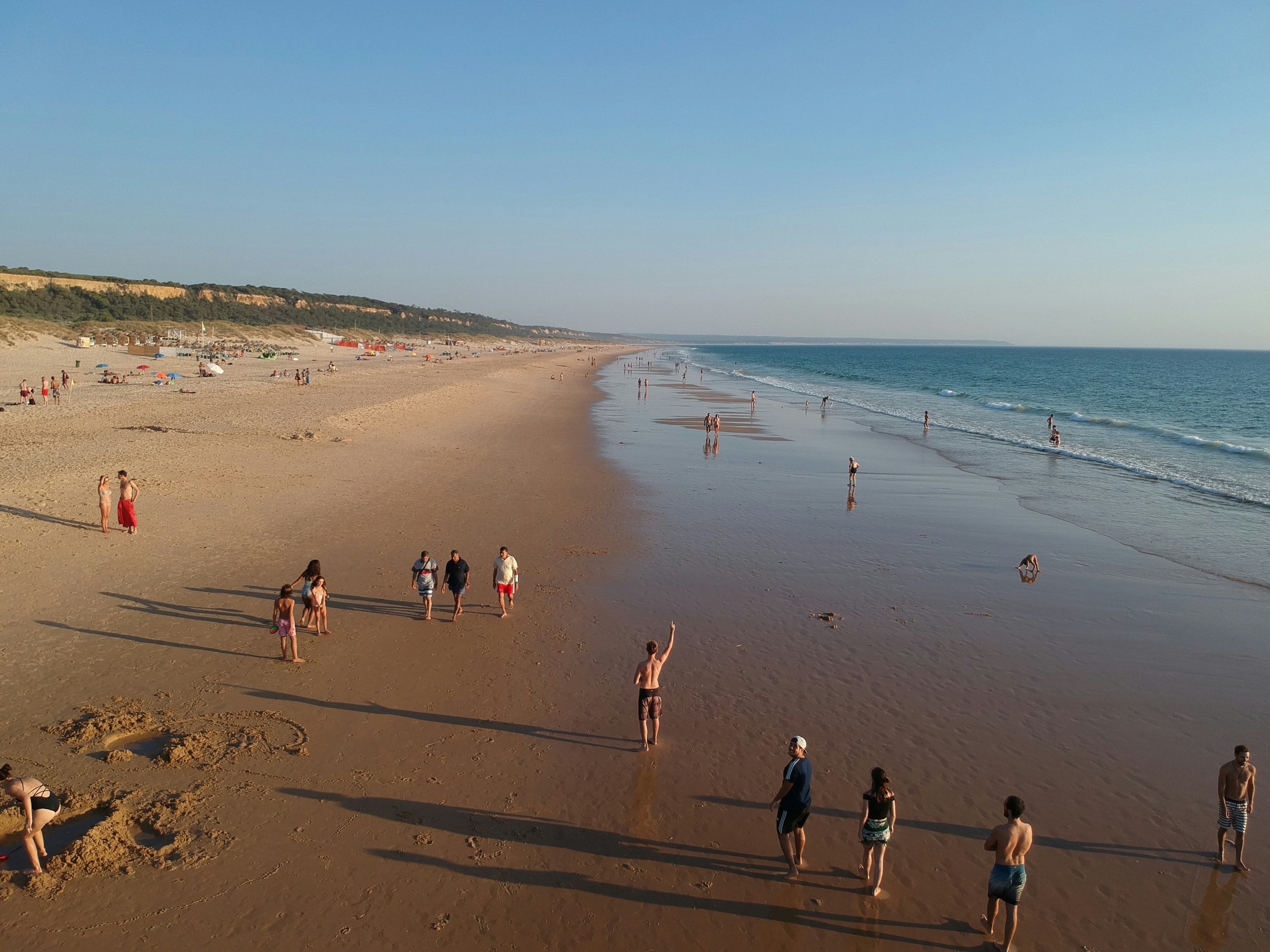 The image portrays a serene beach scene with people enjoying the sandy shore under a clear sky.