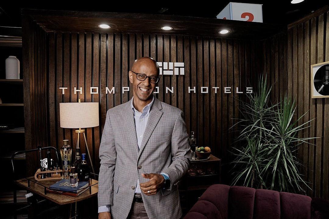 man in suit and glasses smiling at the camera in a wood-paneled office