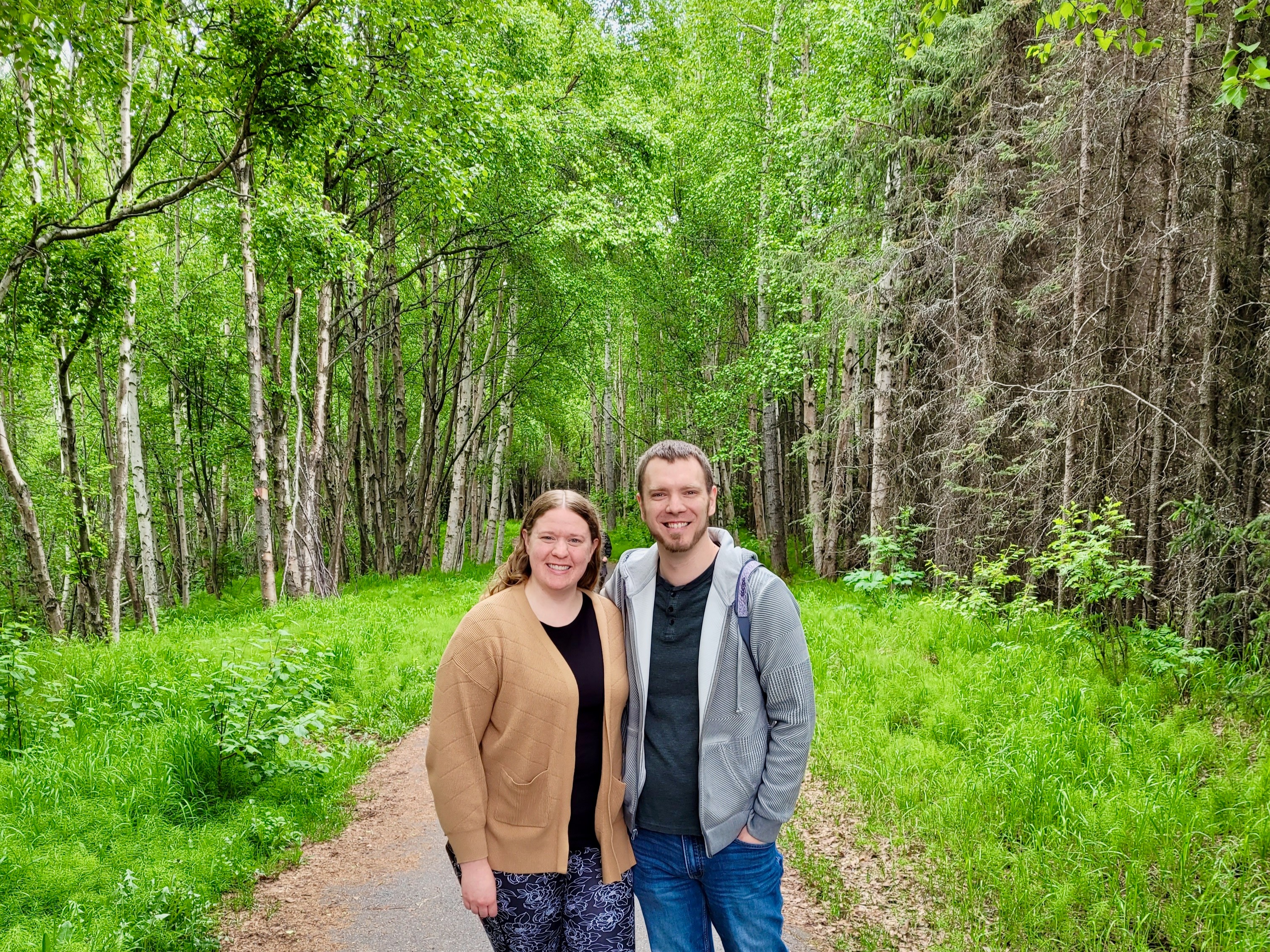 The image portrays two individuals on a forest path, faces obscured by brown rectangles.