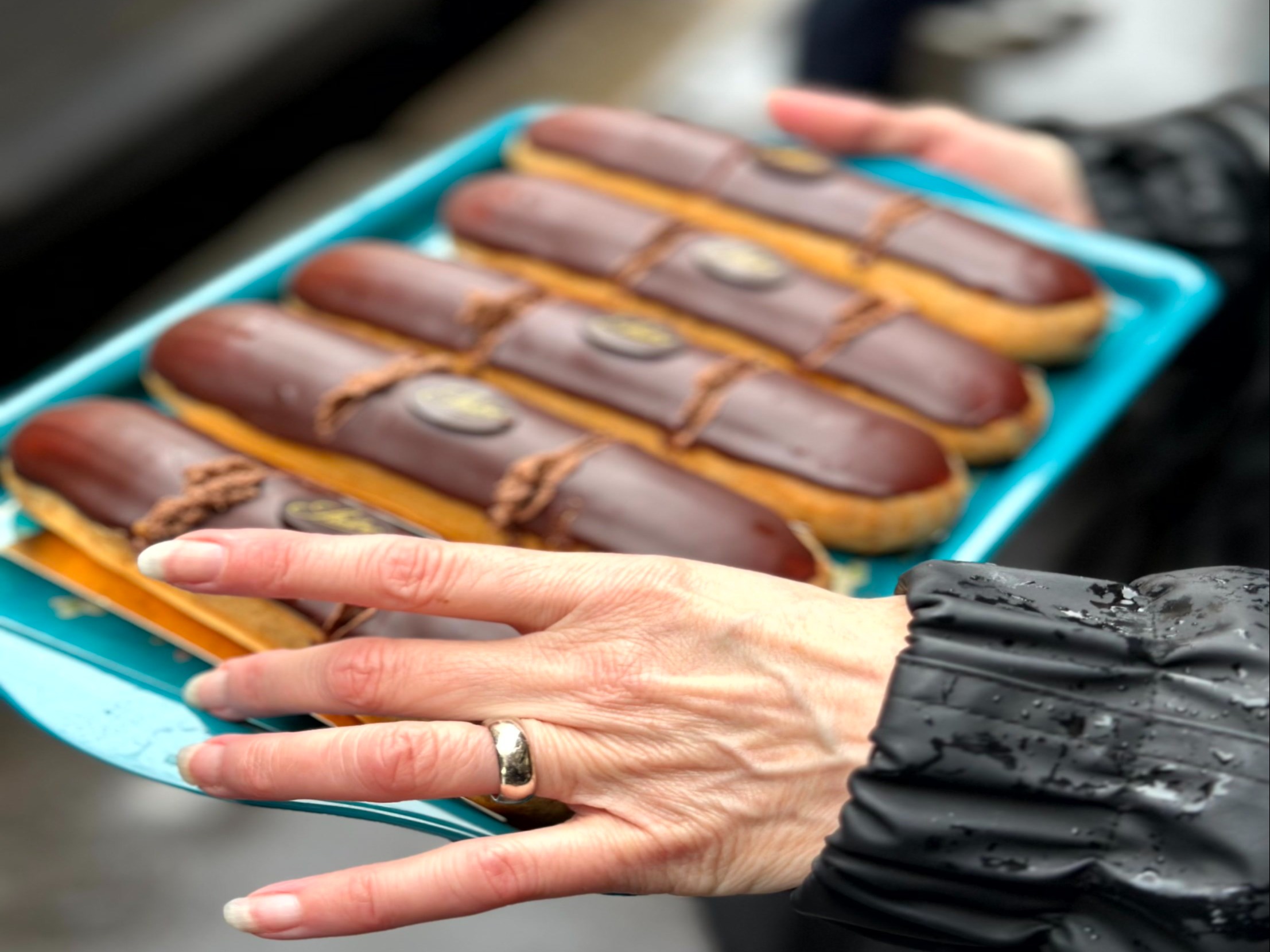 A blue tray with five chocolate-covered eclairs, each garnished with icing and a chocolate piece.