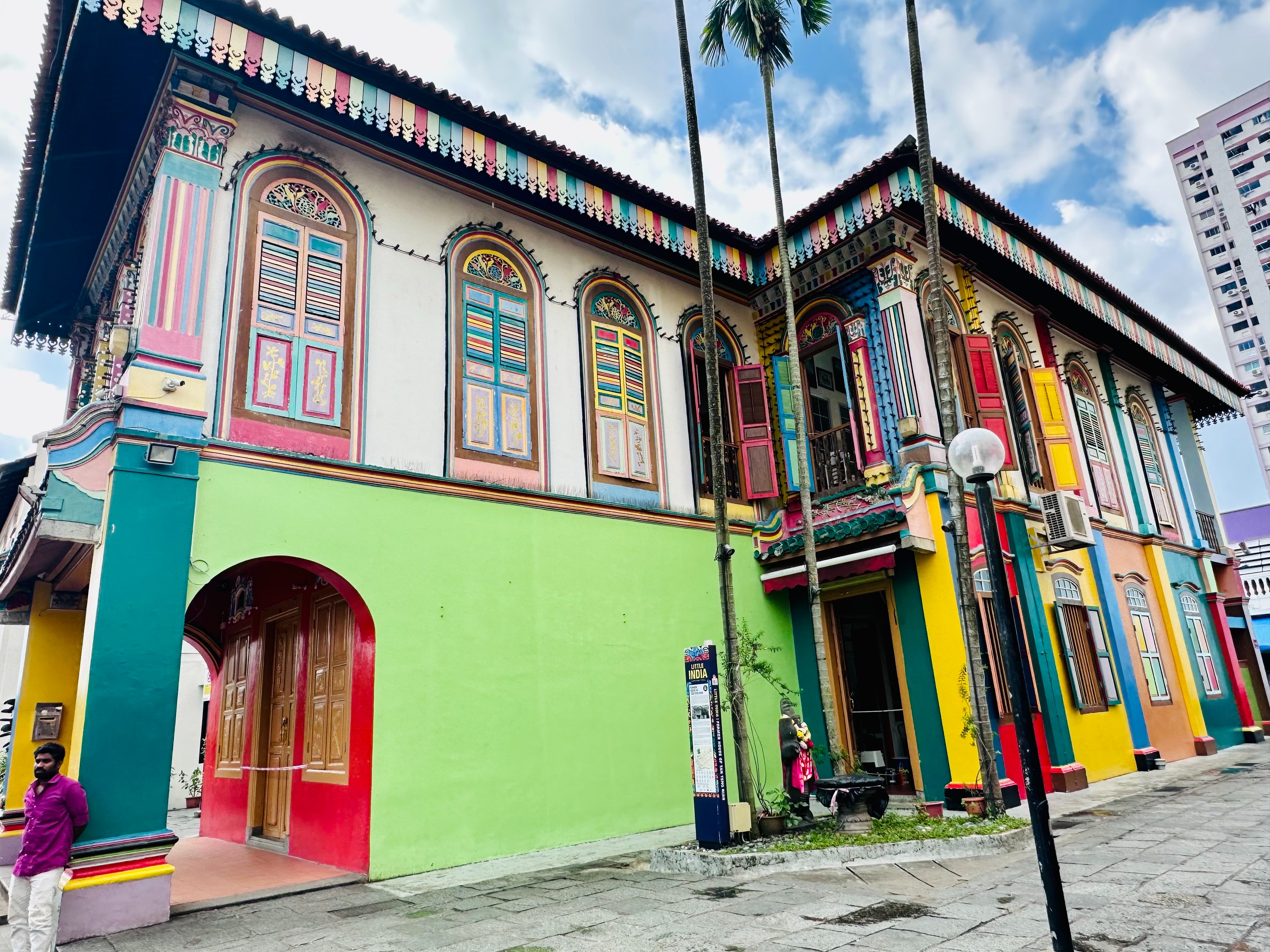 A traditional building with archways painted bright colors, with a modern skyscraper in the background.