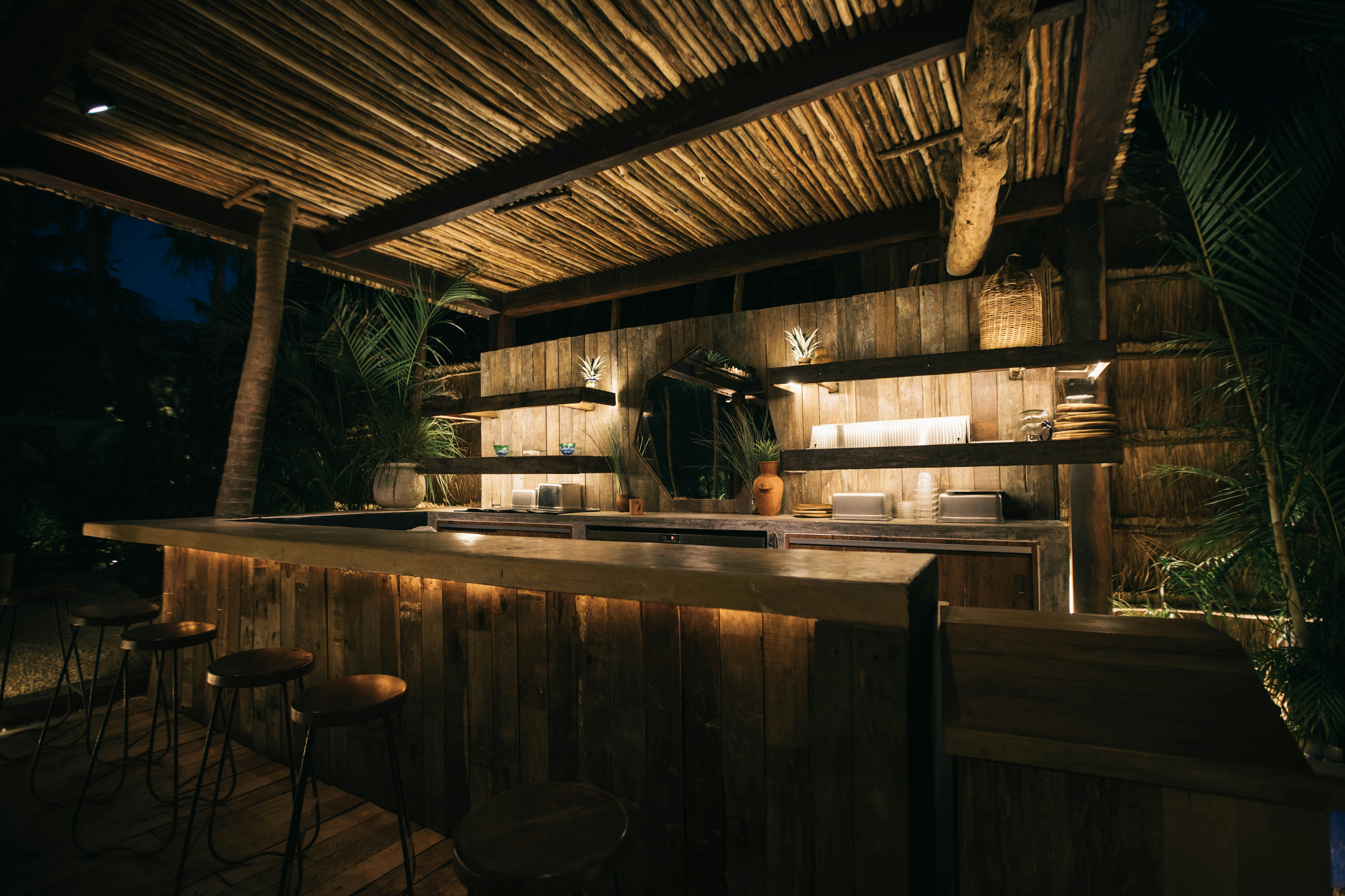 A fancy outdoor wooden bar with a thatched roof and greenery at dusk at NU.