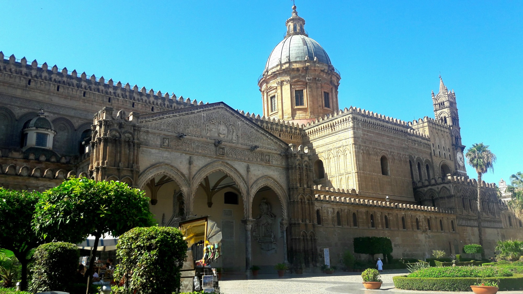 The exterior of a large classical building with a dome, and greenery in the foreground.