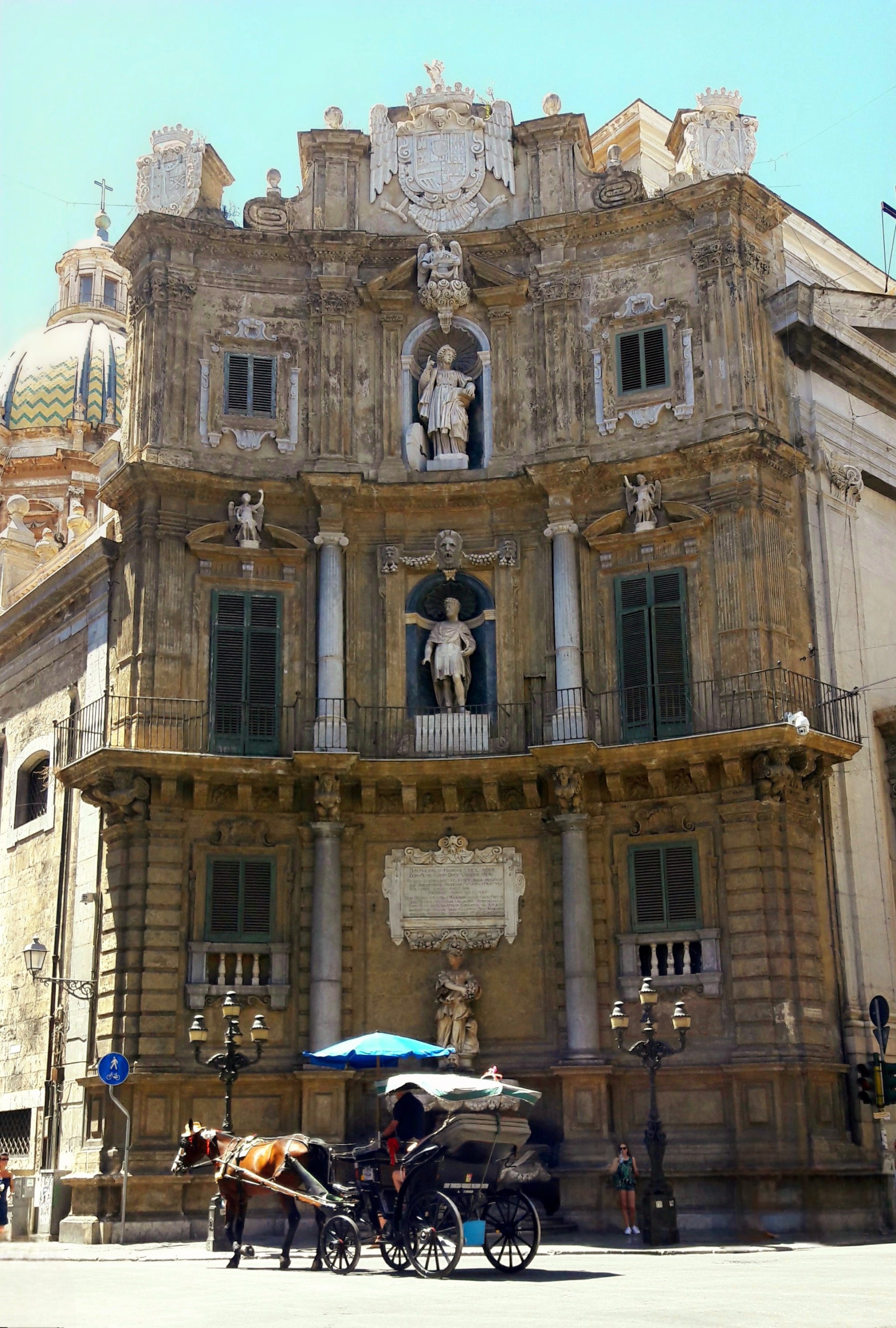 A three-story stone building with ornate sculptures at Quattro Canti