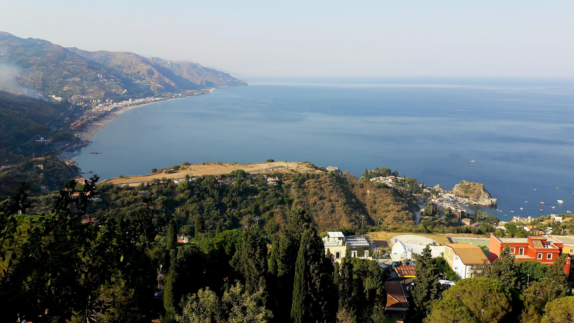 Aerial view of the ocean next to green trees and hillsides.