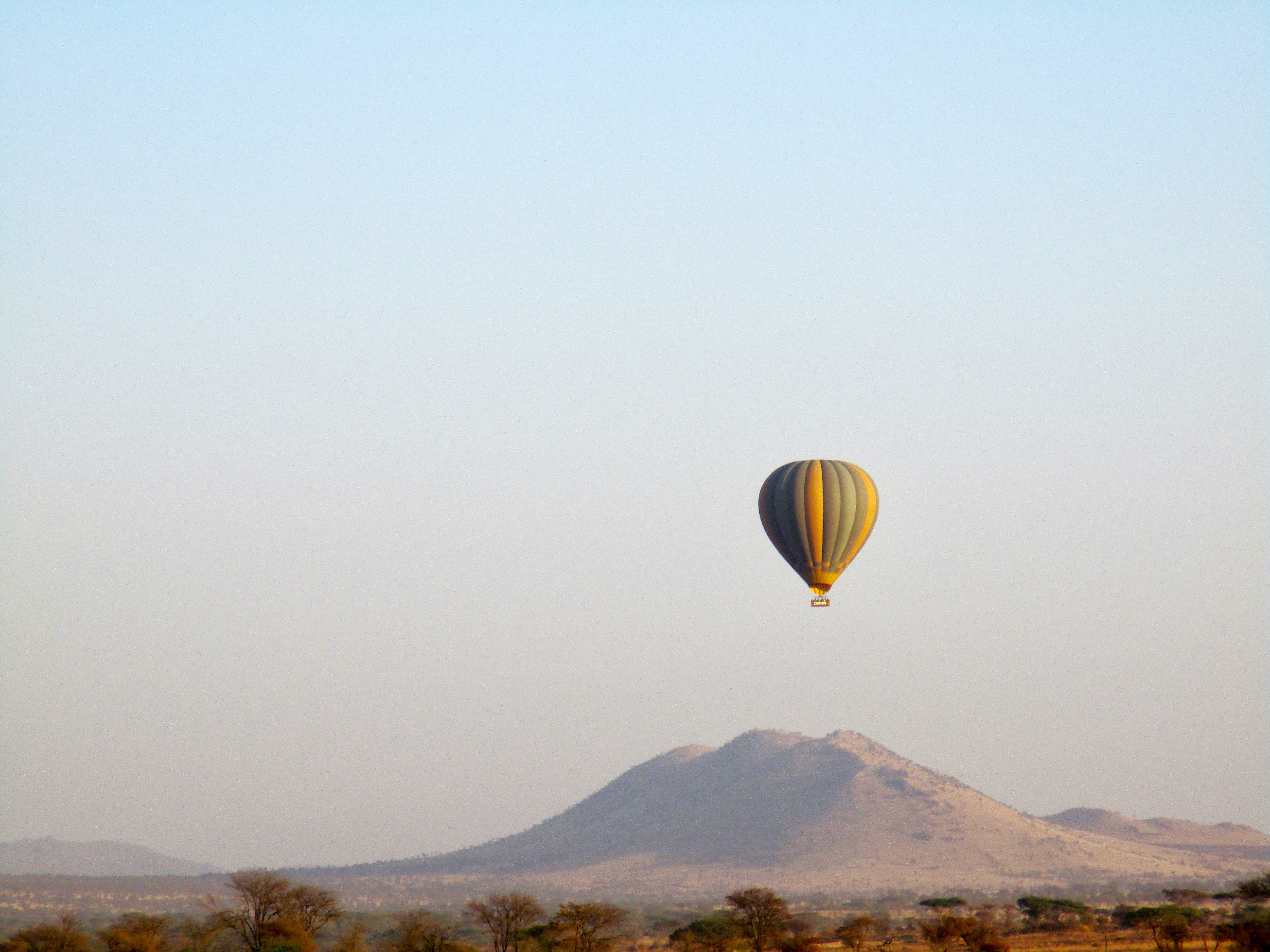The image features a hot air balloon soaring over a mountainous terrain under a clear sky.