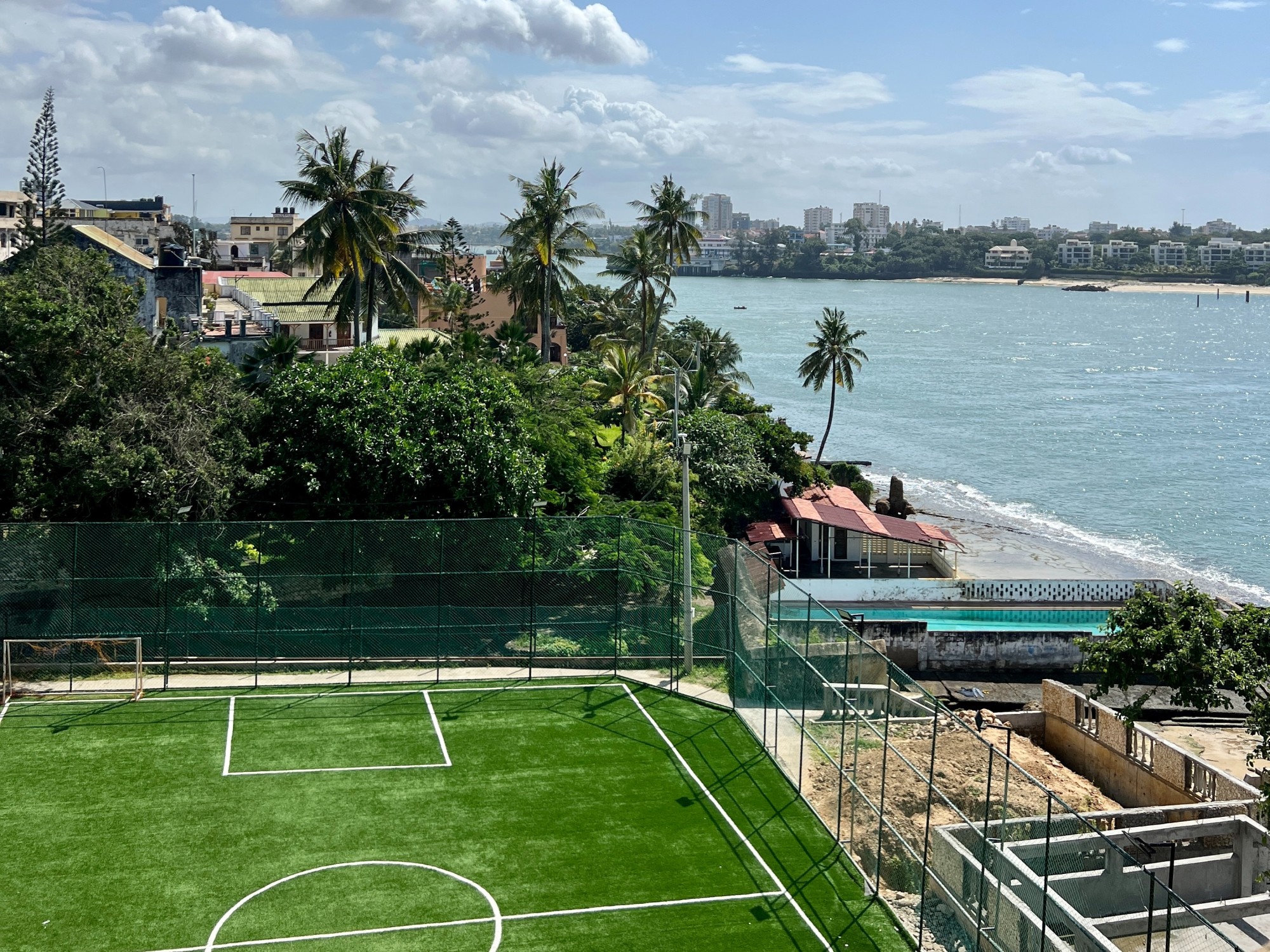View of tennis court and beach with buildings.