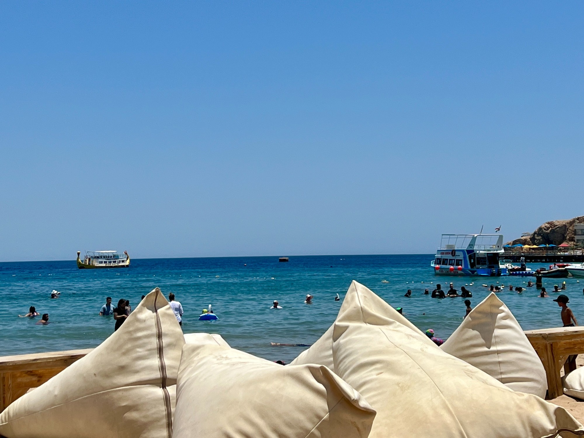 View of ocean from beach with boats and people swimming.