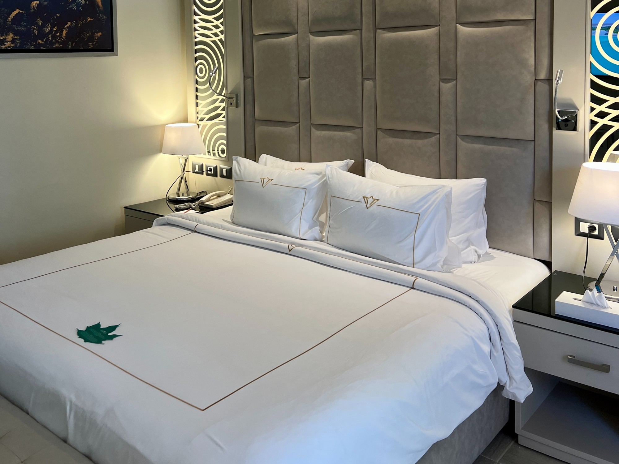 A bed with white bedding and tall, gray headboard in a hotel room.