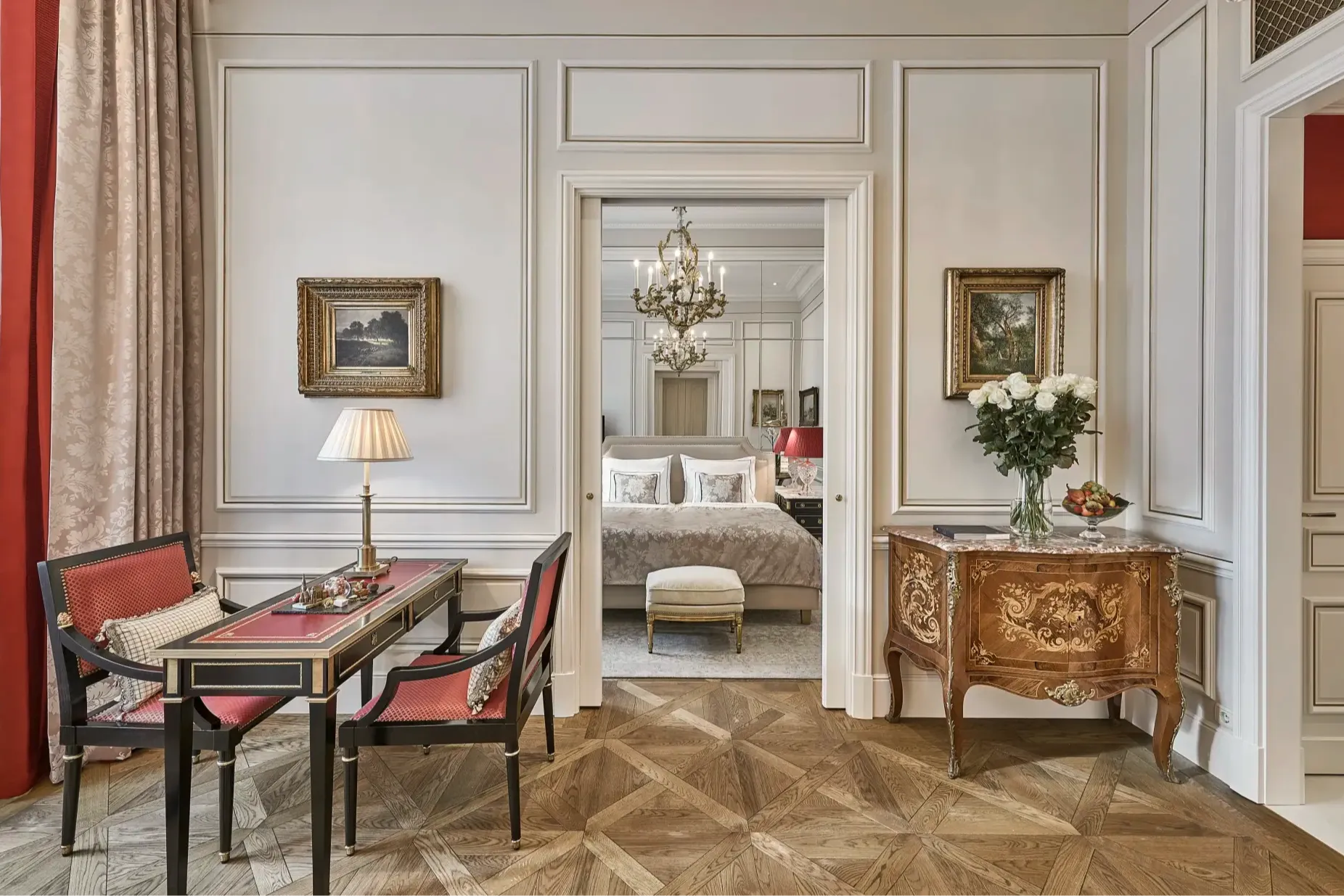 a fancy hotel room with wooden floors, red drapes, and a writing desk with red chairs
