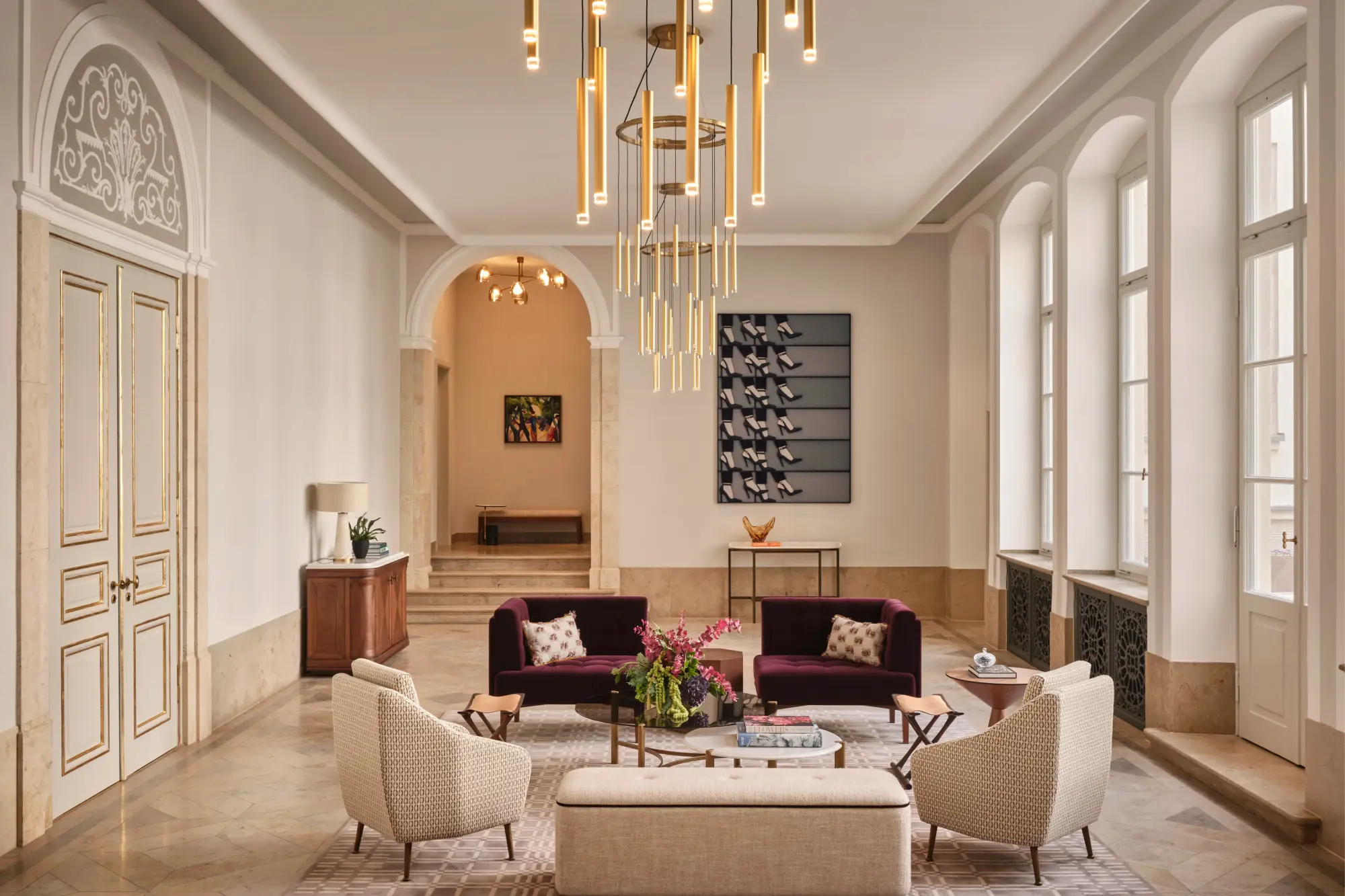 a stately living room with gleaming white walls, a gold chandelier, and purple and white couches