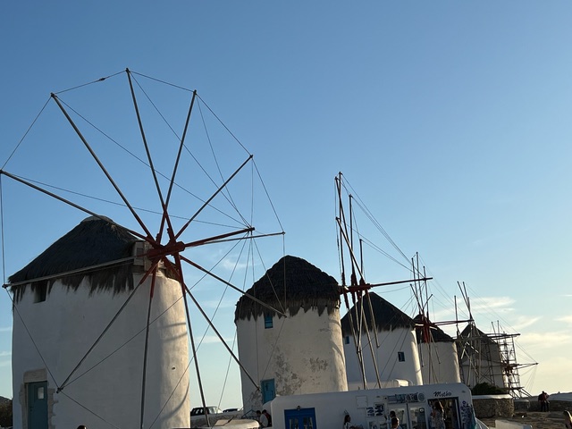 A line of old-fashioned windmills with thatched roofs and wooden spokes.