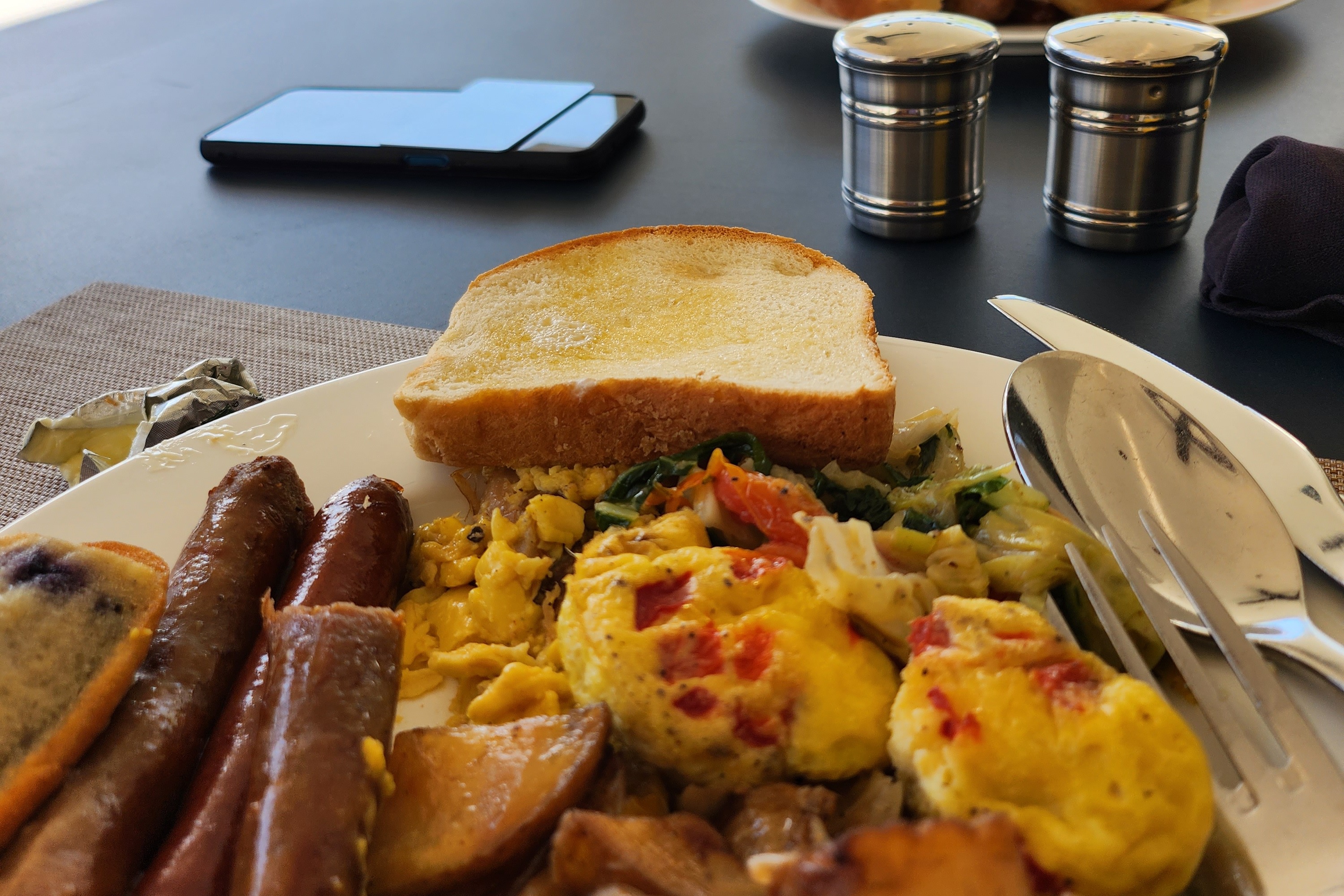 A close-up of a plate of sausages, toast, scrambled eggs and potatoes on a table.