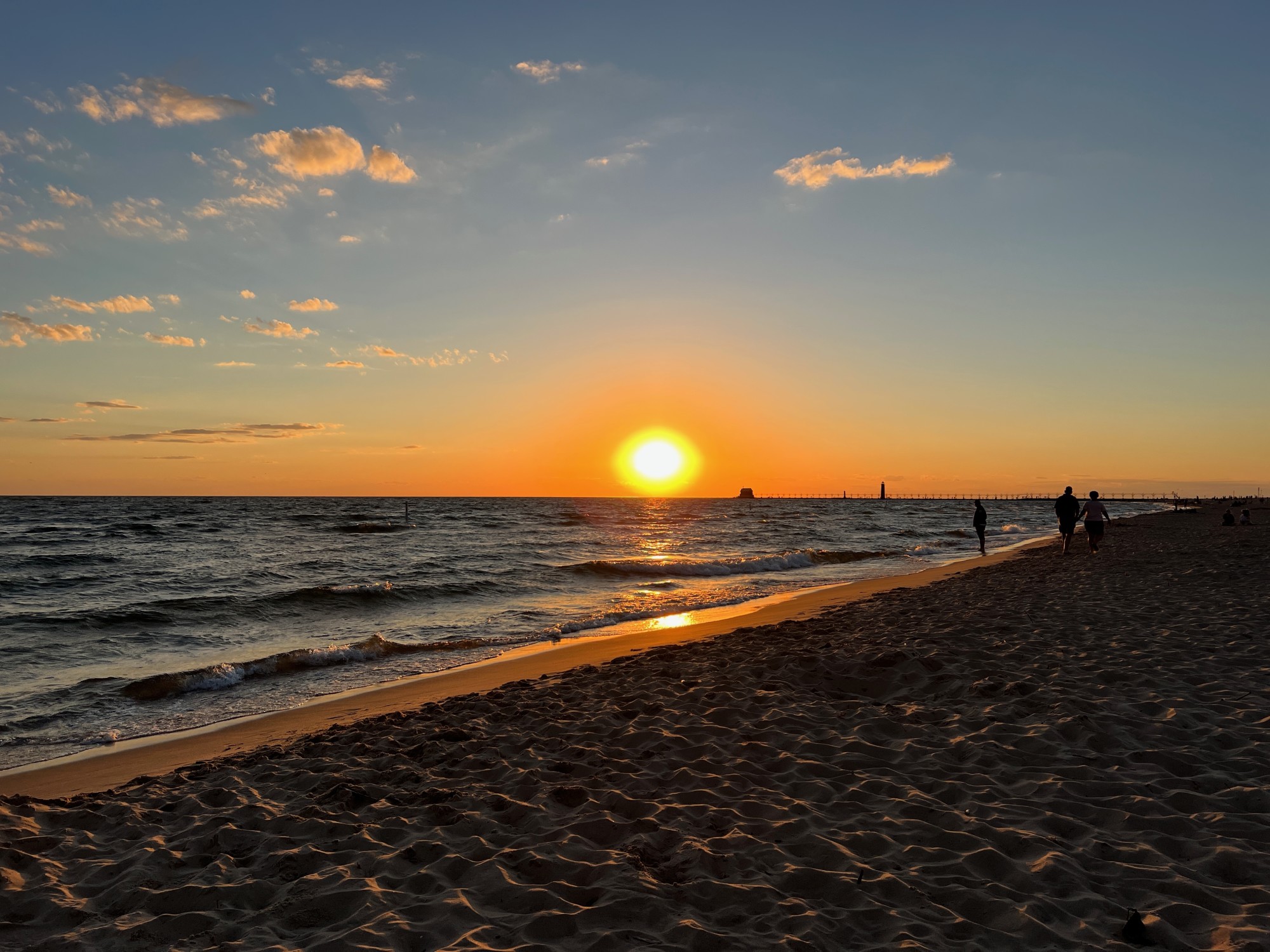 Sunset over Lake Michigan with people walking along the shore on a clear sky evening.