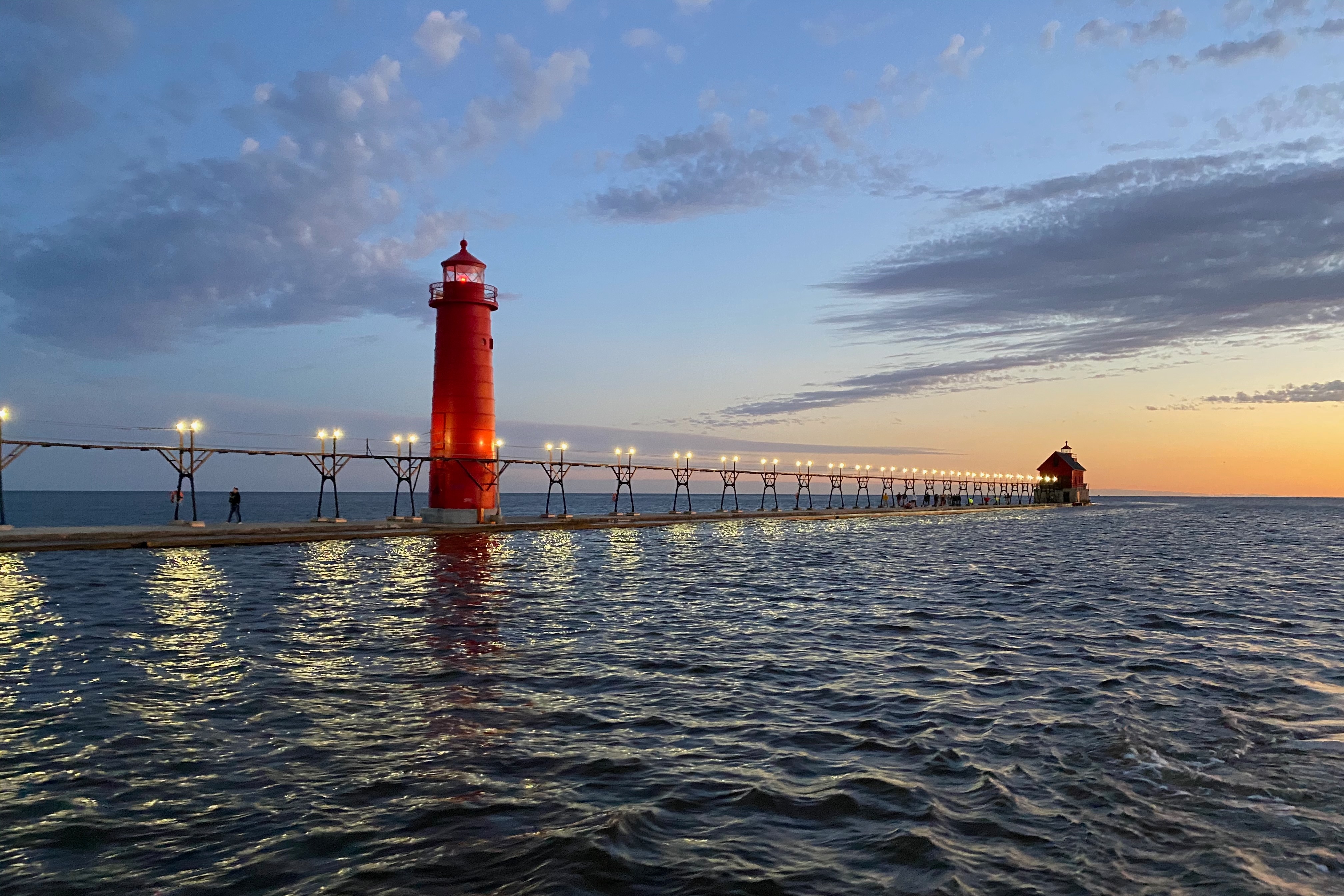 View of the red lighthouse and ocean at Grand Haven Pier at sunset.