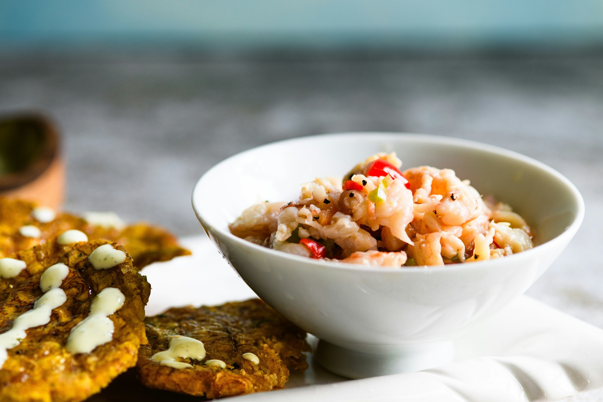 Chopped seafood in a bowl on a plate next to fritters.