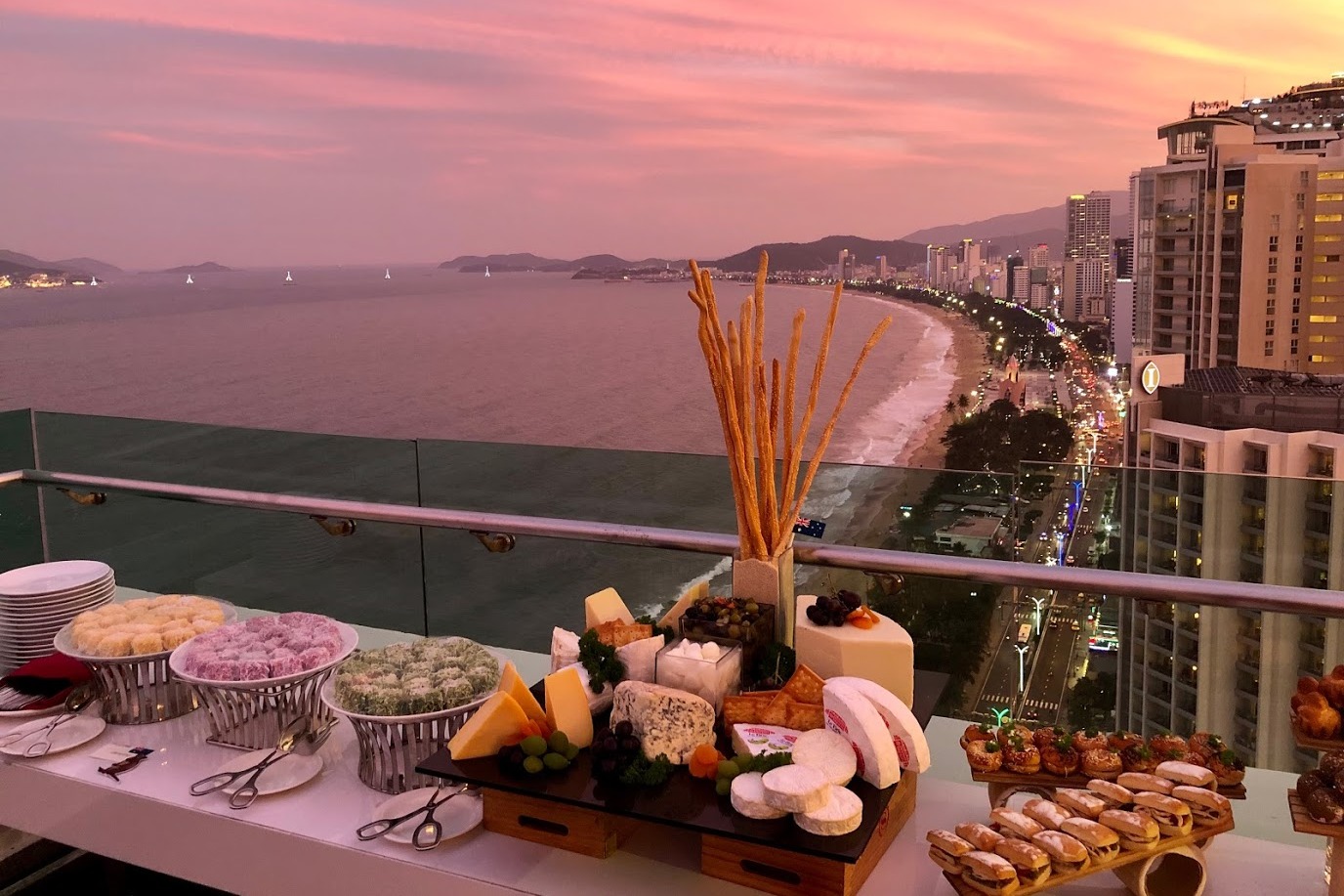The view from Altitude Rooftop Bar at sunset overlooking the coastline and ocean with a display of food.