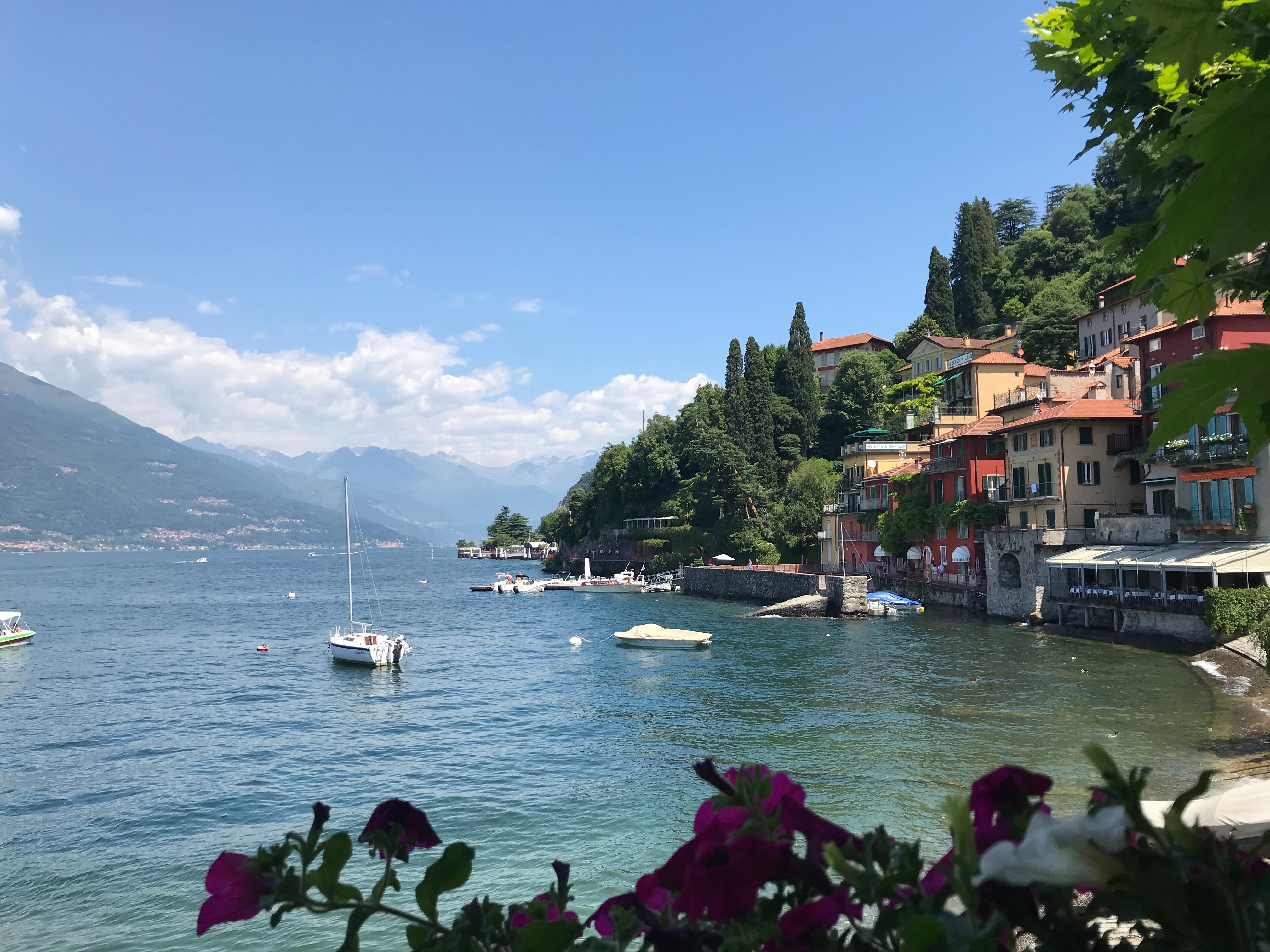 A picturesque lakeside view, where boats gently float by colorful buildings under a clear blue sky.