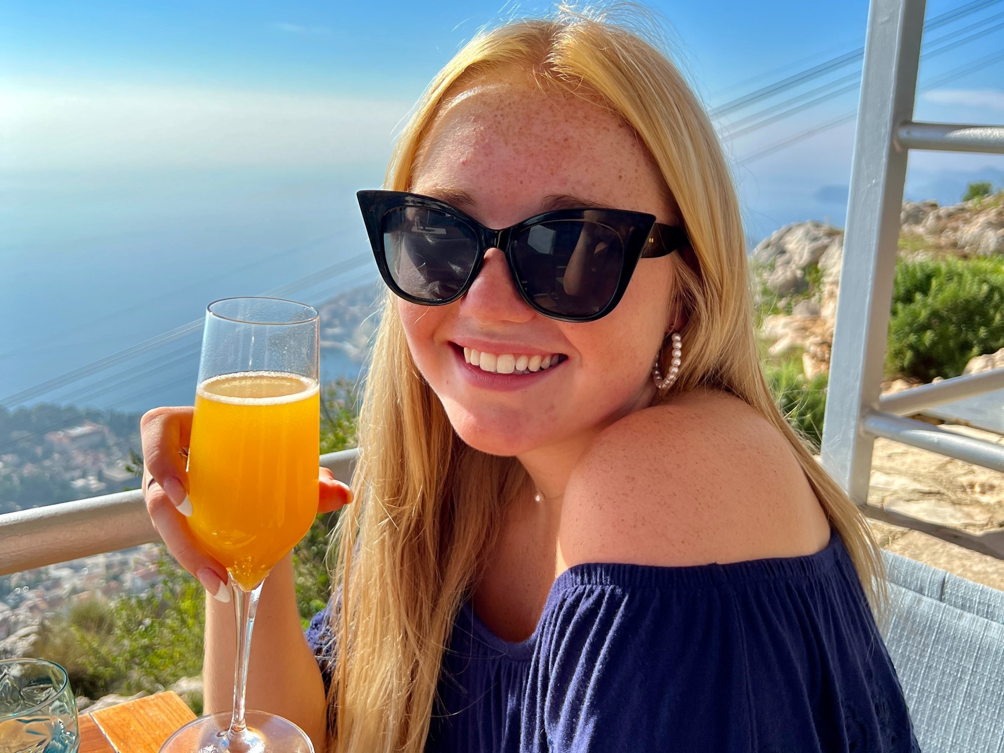 A woman holding a stemmed glass of an orange drink.