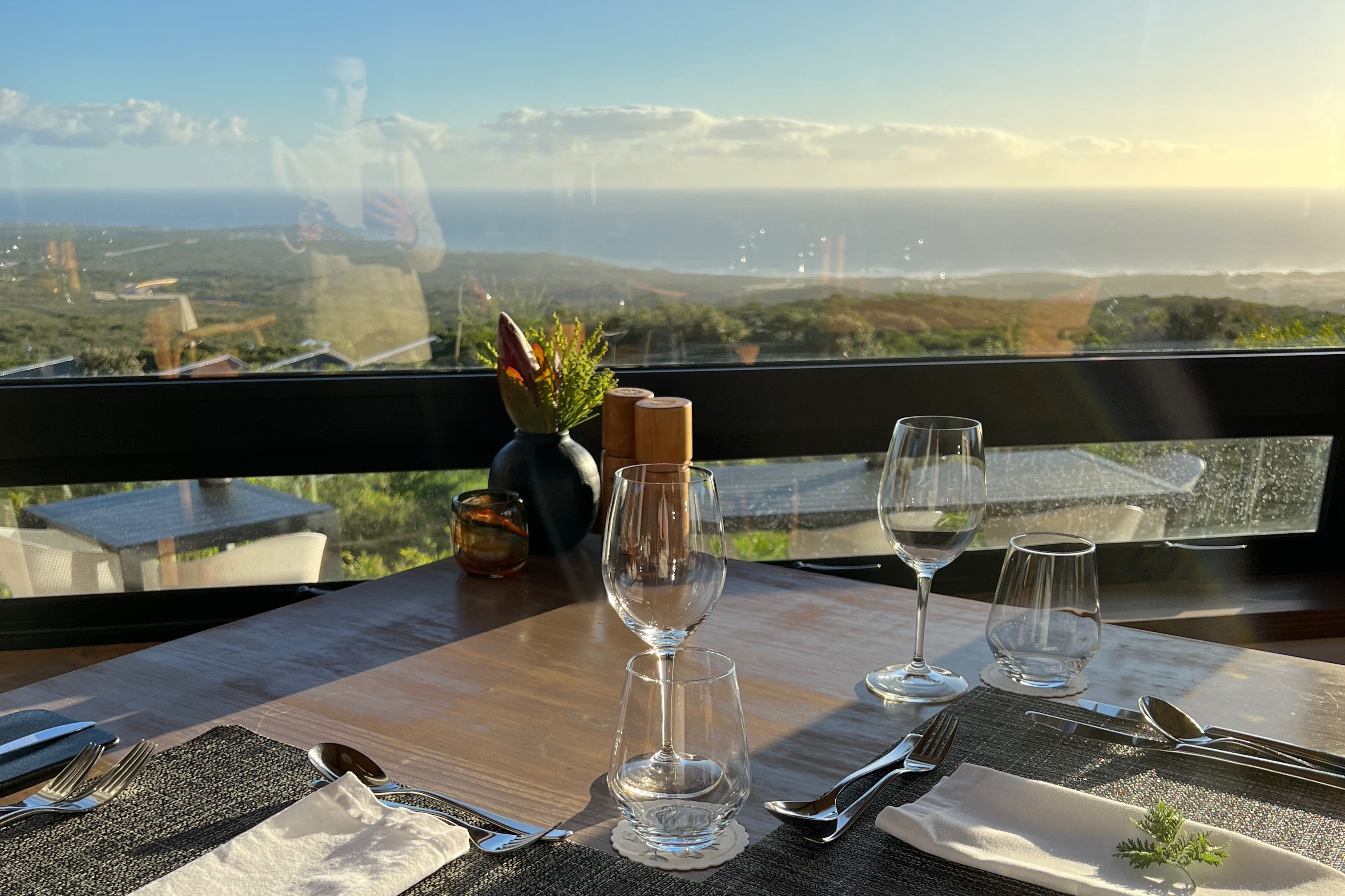 A dining setup with wine glasses overlooking a beautiful view of llush green landscape and the ocean.