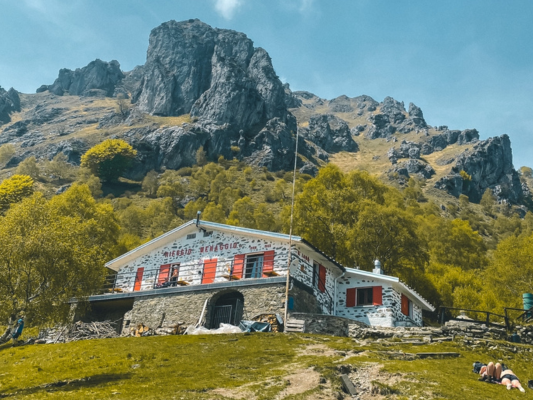 A serene mountain refuge sits beneath a clear blue sky, backed by rugged peaks.