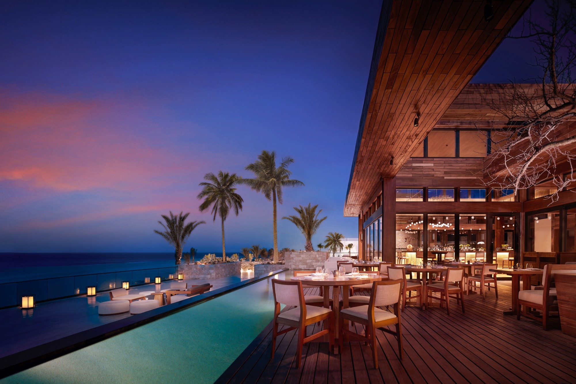 evening on a terrace overlooking pool and see with wood deck and restaurant seating