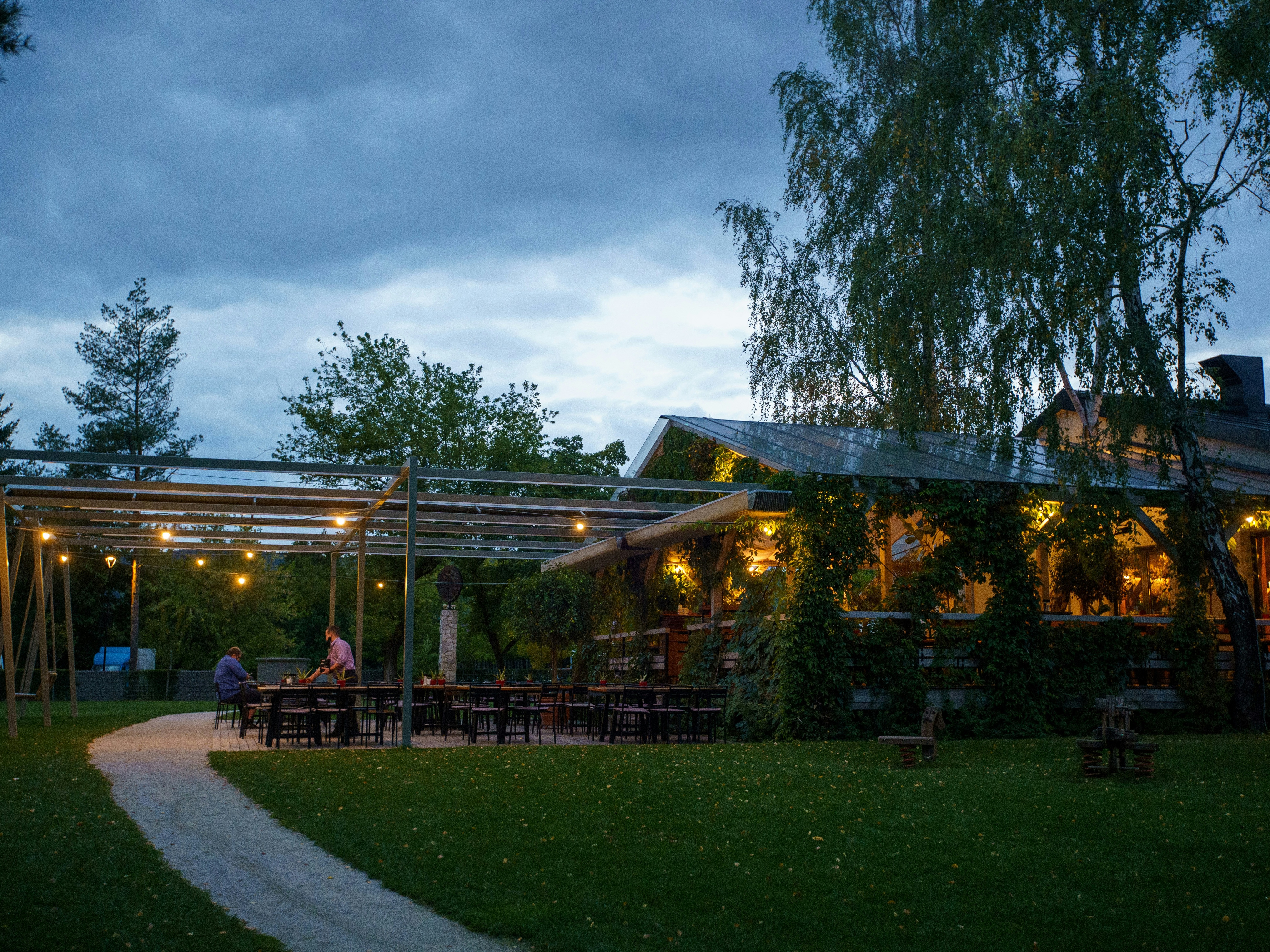 An enchanting evening at a restaurant with patrons dining under lit canopies amidst greenery.