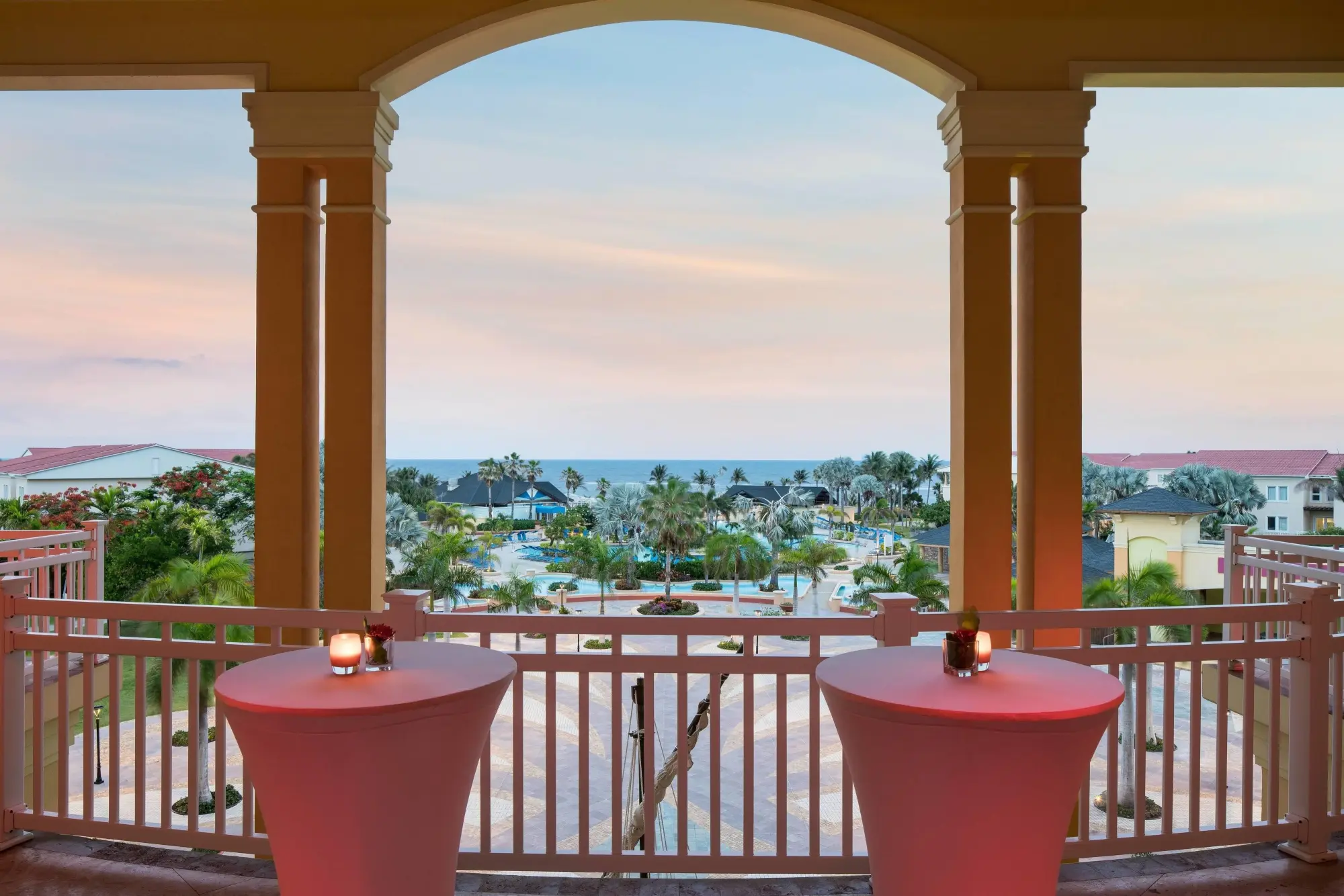 Viewpoint from a balcony at St. Kitts Marriott Resort & The Royal Beach Casino: Twin cocktail tables stand before a railing with the resort grounds and ocean in the background