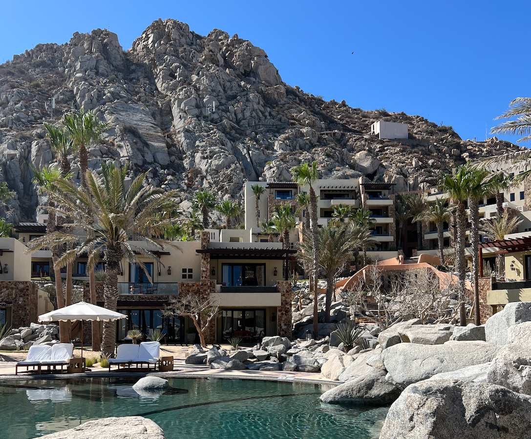 The Waldorf Astoria pool surrounded by rocks, tan-colored buildings and mountains.