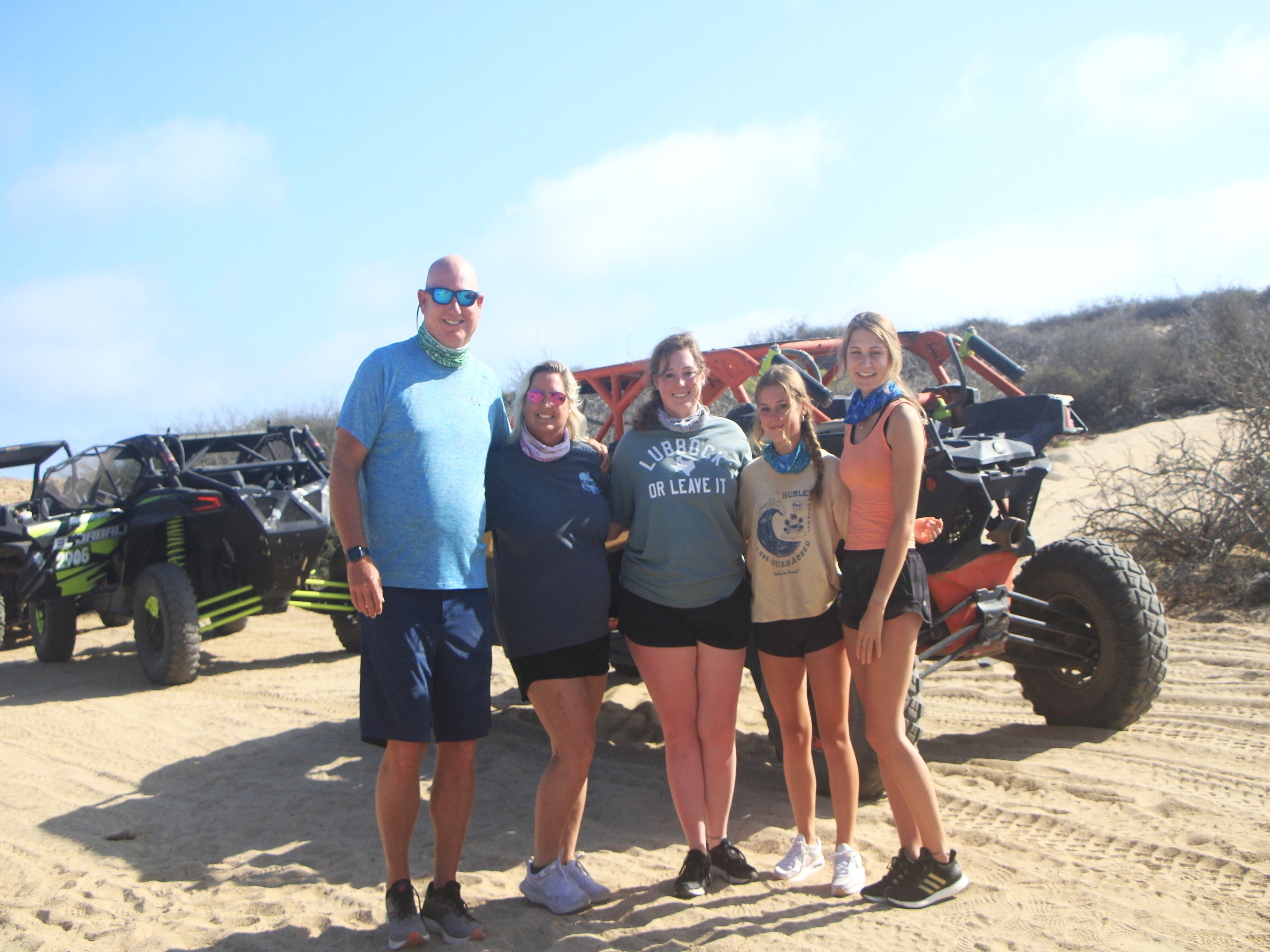 A family standing by an off-road vehicle on sandy terrain.
