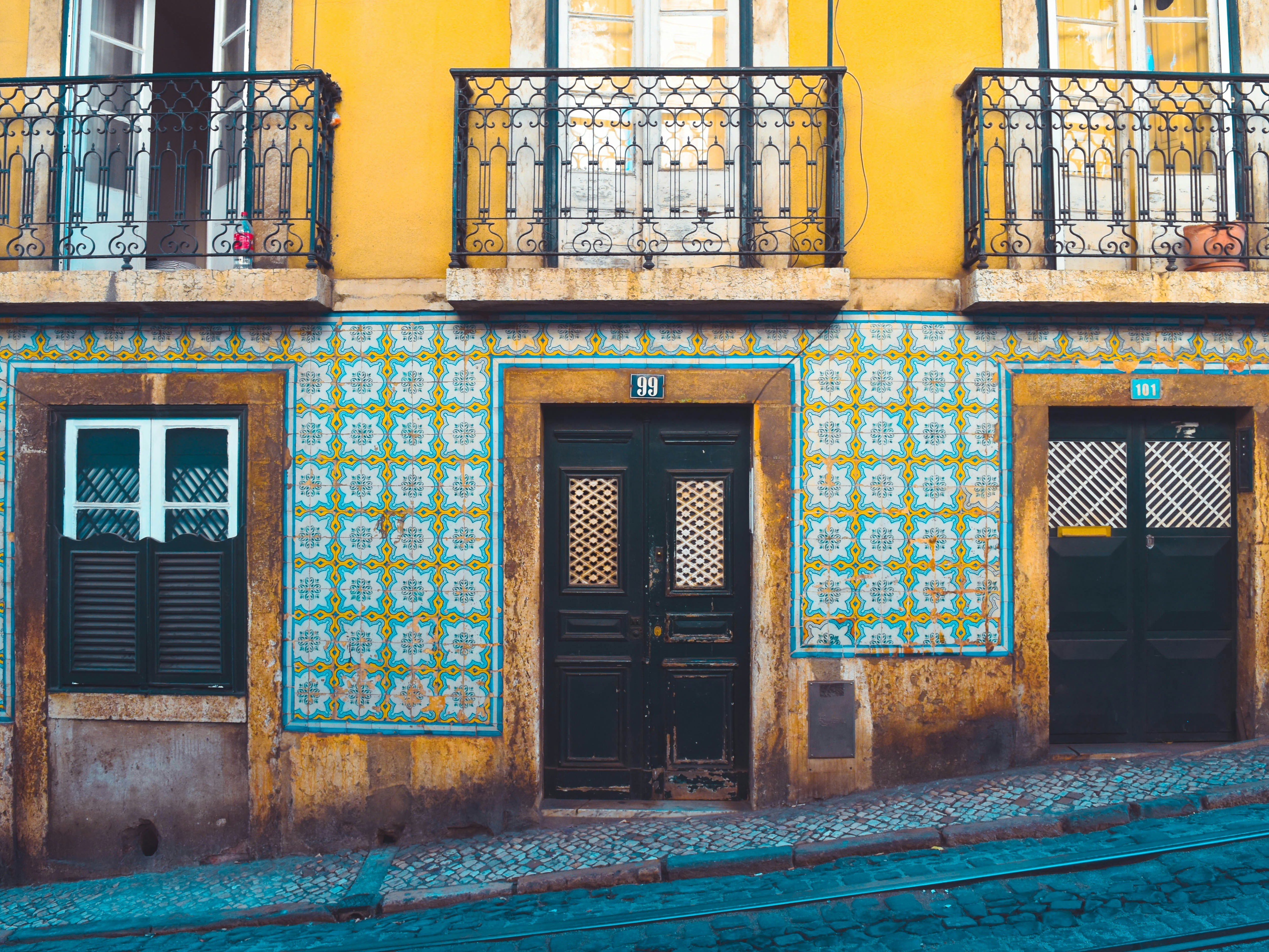 The image displays a colorful, tiled facade of a building with two doors and windows, set against cobblestone streets.