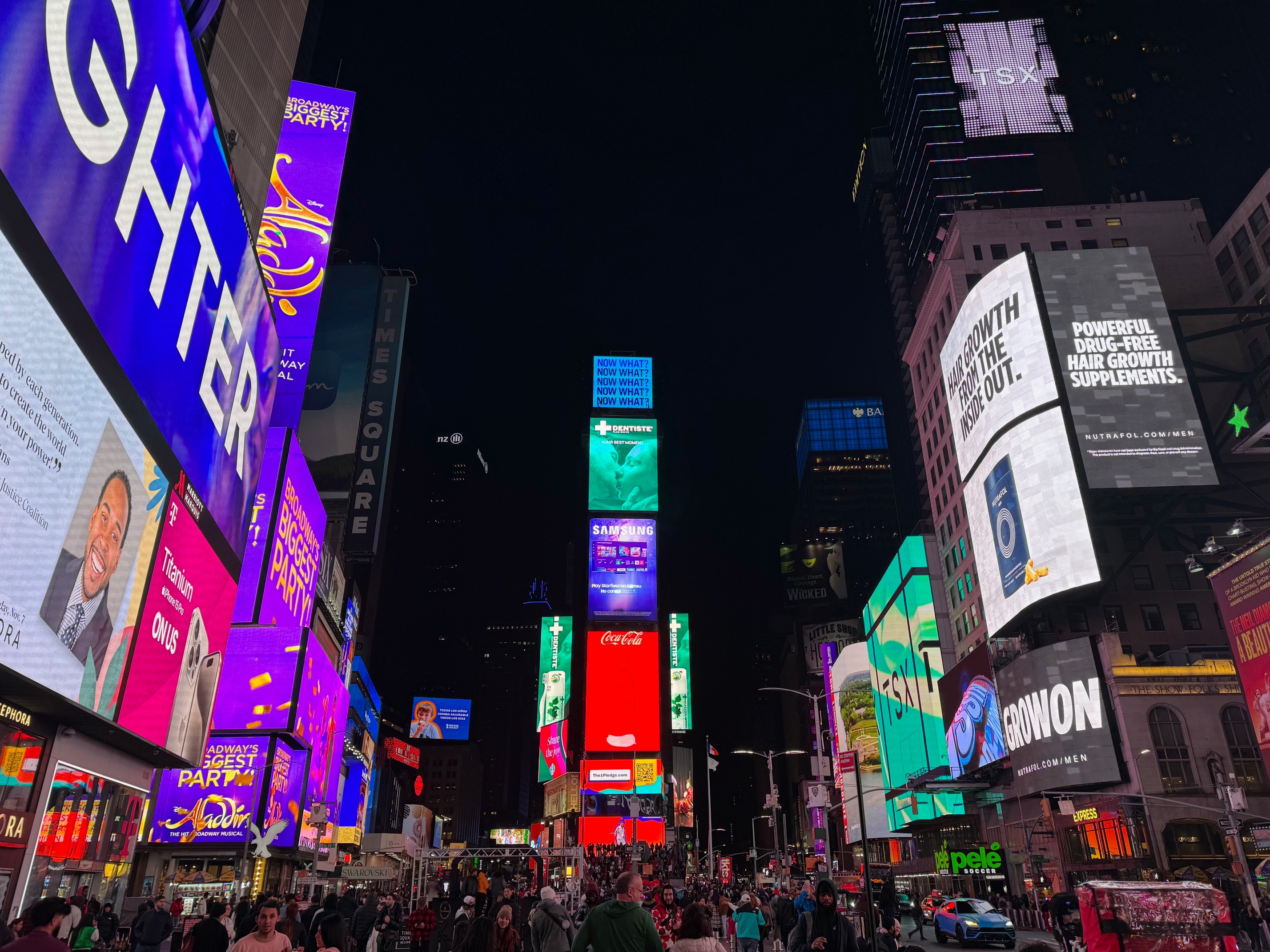The image portrays Times Square at night, alive with crowds and radiant with vivid billboards.