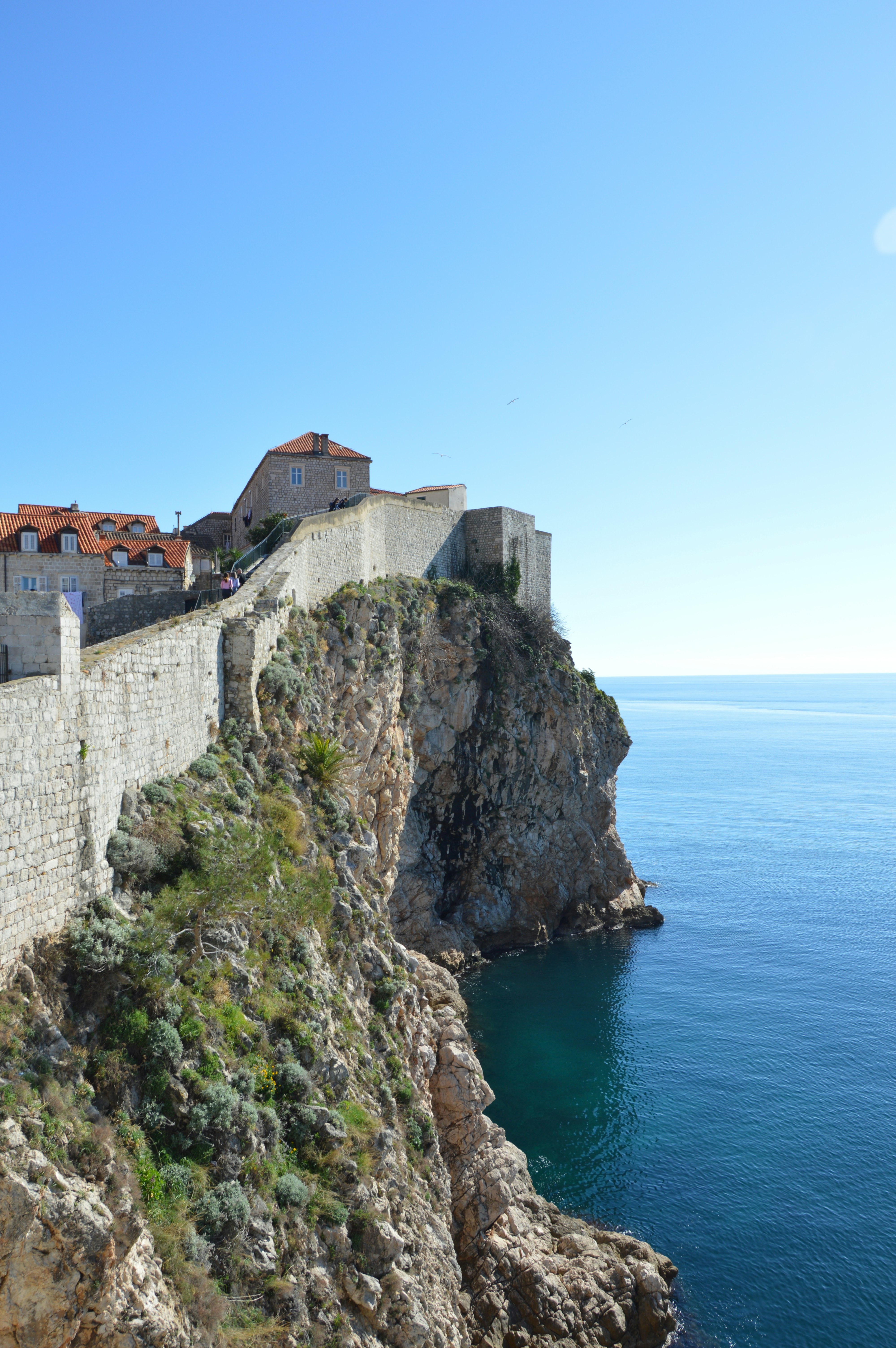 A view of Dubrovnik's Old Town wall lining the cliff and coastline of Croatia's capital city on a sunny day.