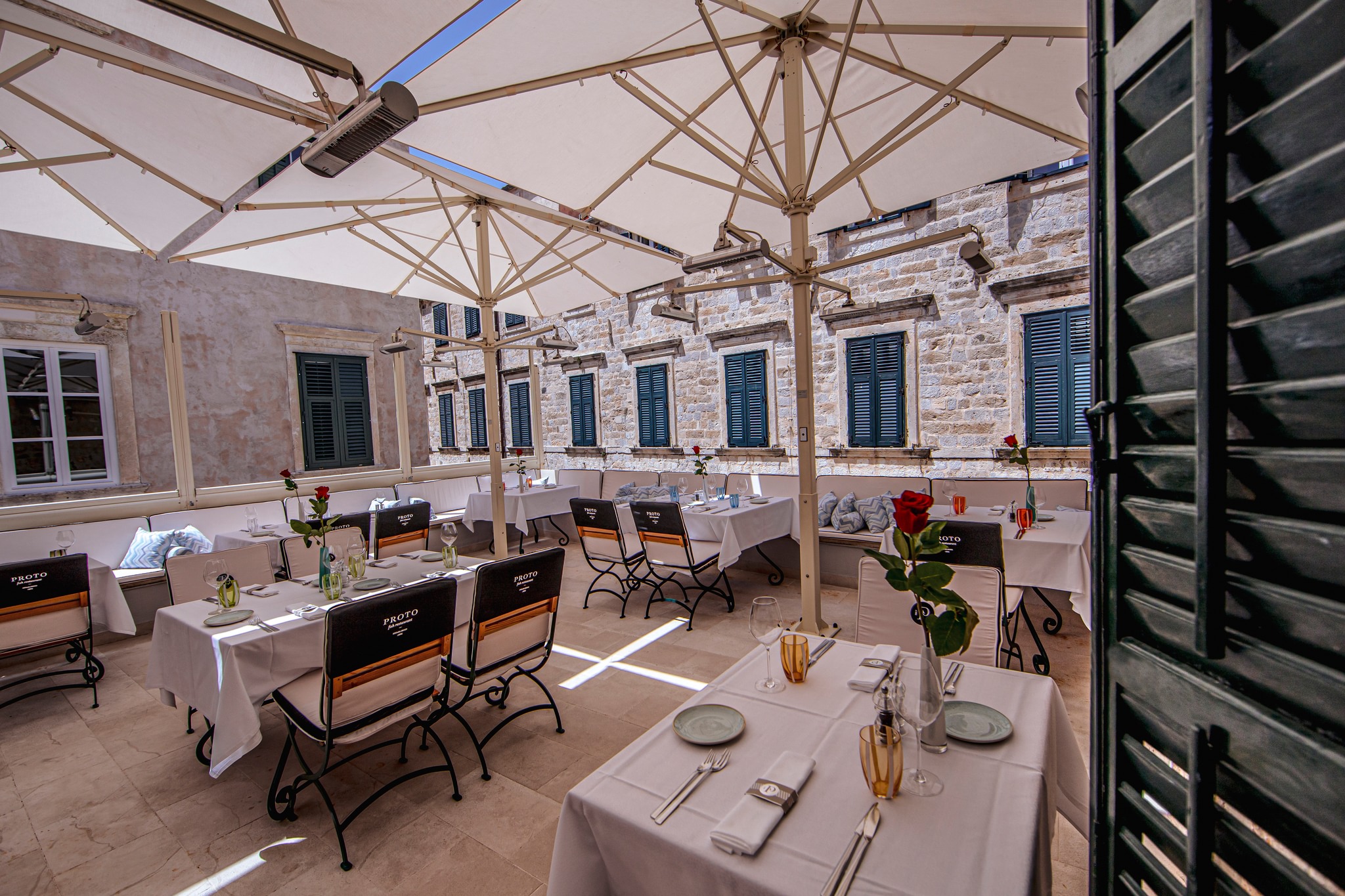 Tables and chairs set at a local restaurant, with white umbrellas shielding the dining area from the sun.