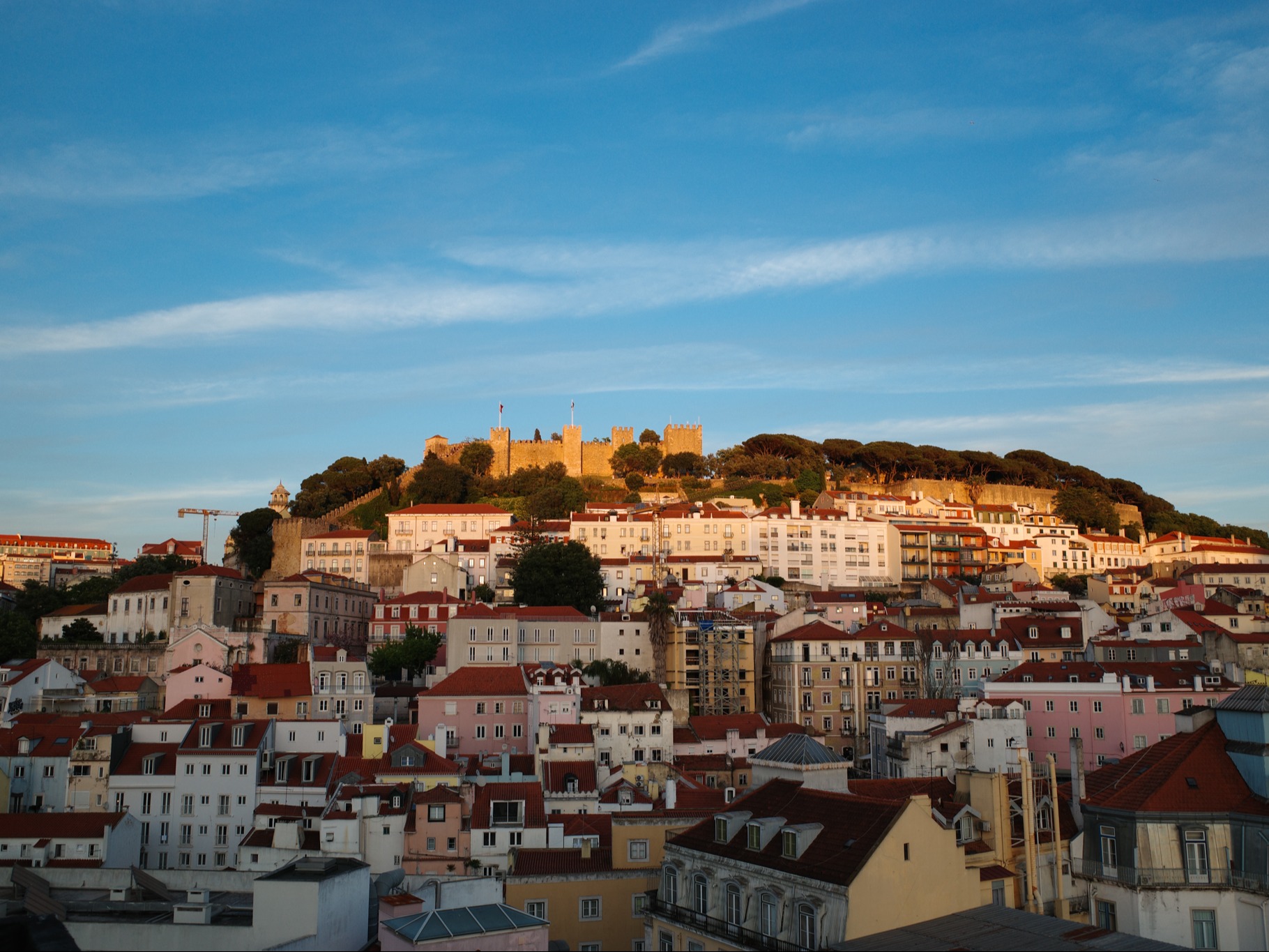 The image depicts a stunning sunset view over a city, highlighting the city’s vibrant architecture and the prominent castle on a hill.