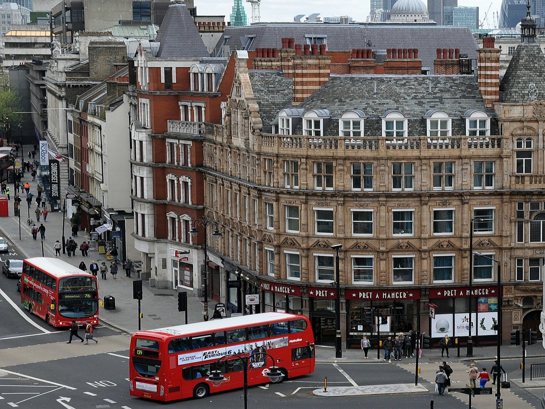The image portrays a vibrant city street bustling with red double-decker buses and pedestrians, framed by classic architecture.