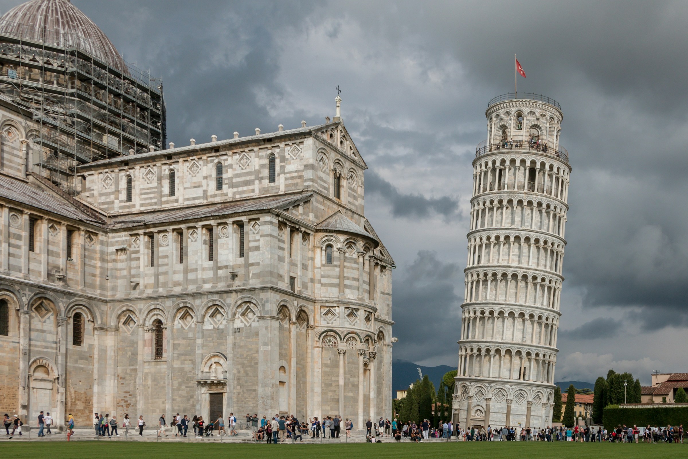 The Leaning Tower of Pisa and a white marble cathedral to the left of it on a gloomy day.