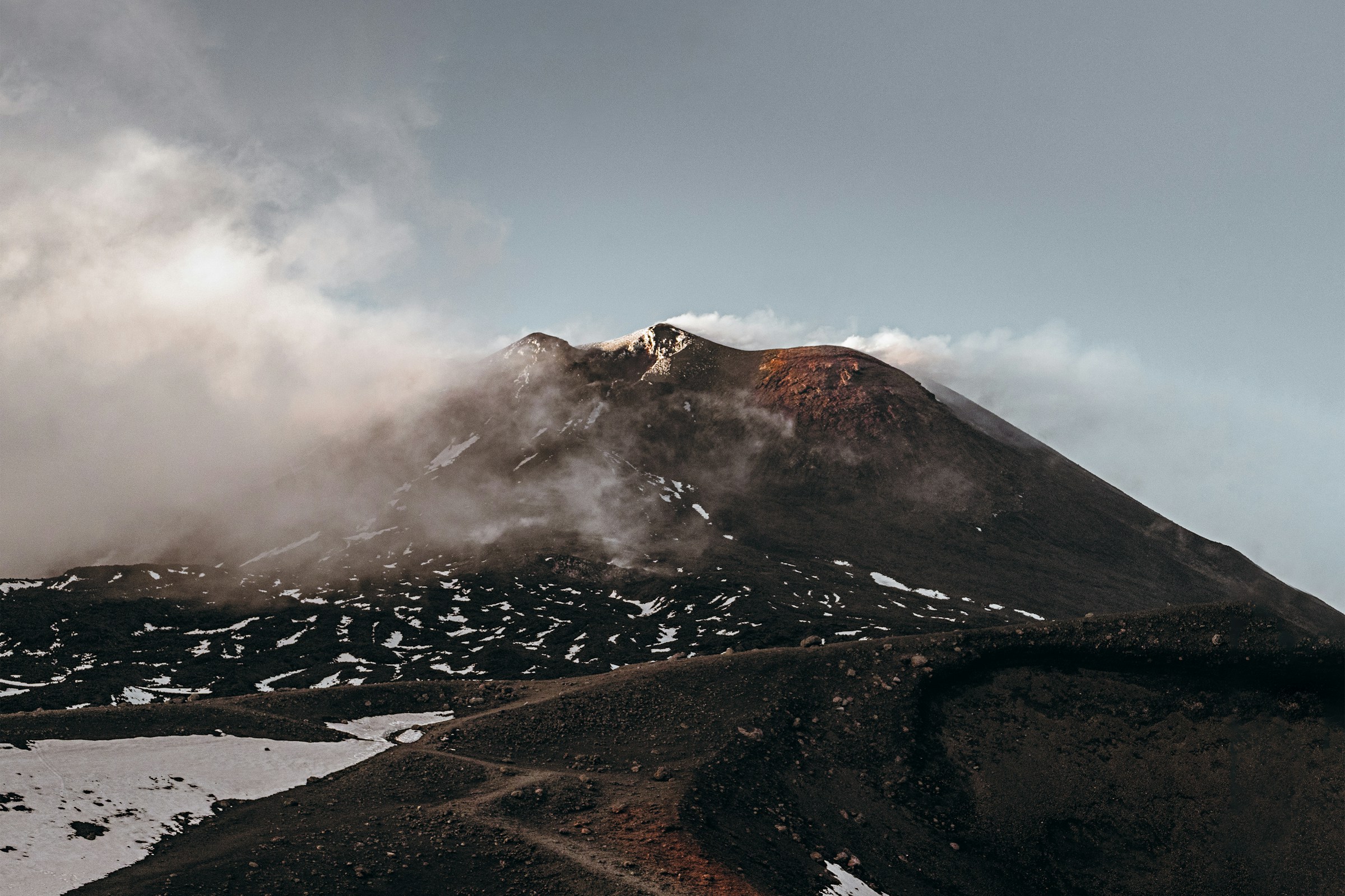 Mount Etna's peak on a partially cloudy day with fog rolling in over the peak.