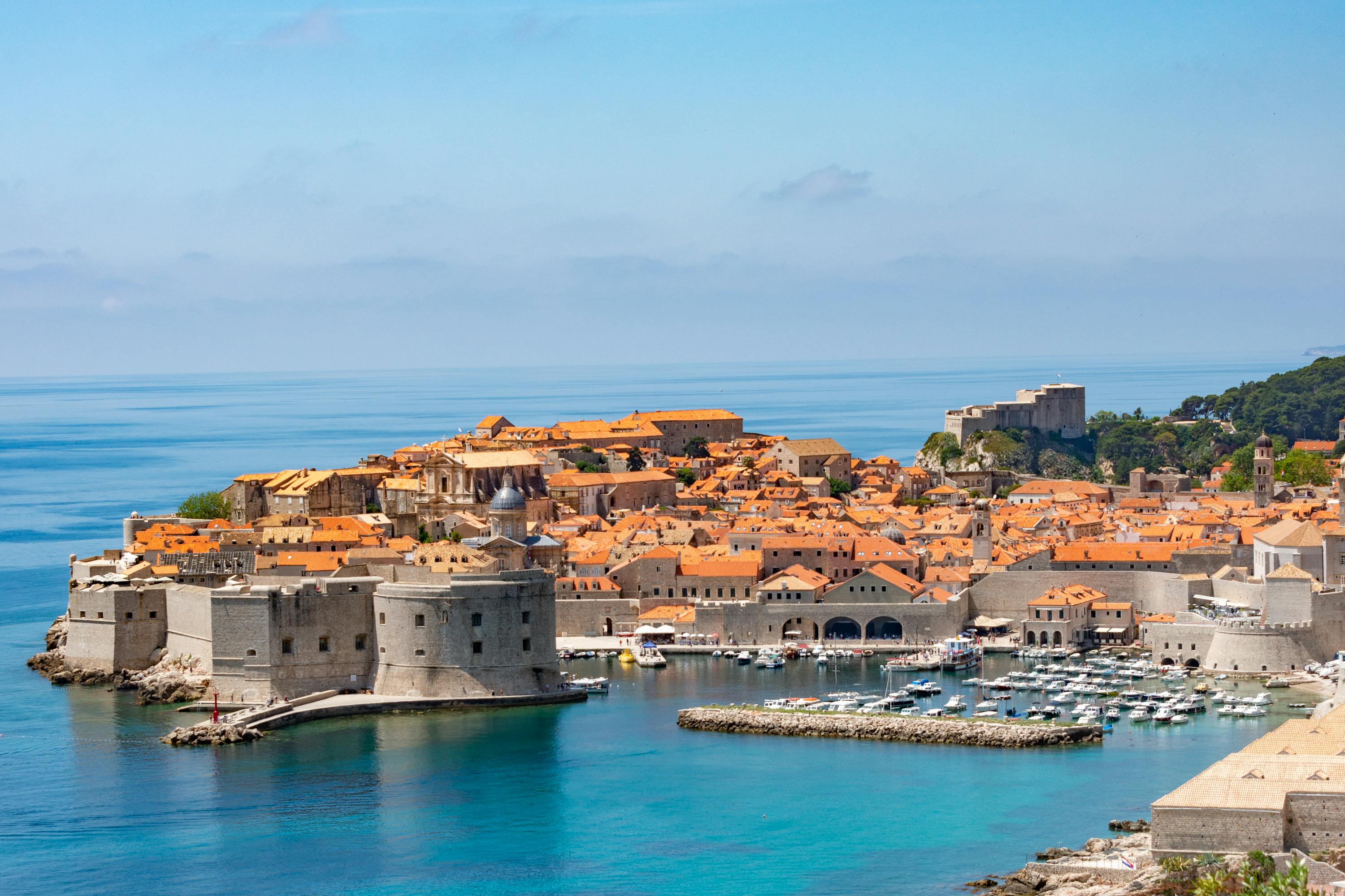 View of Dubrovnik Old Town, an old town on the water with stone buildings with orange roofs.