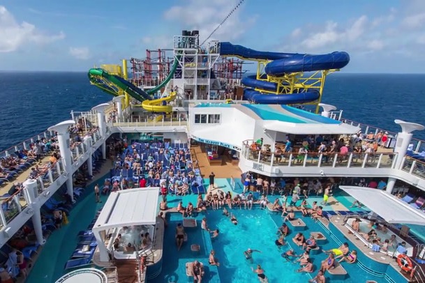 An aerial photo of the cruise's pool deck full of people enjoying swim-up bars, water slides and various lounge areas.