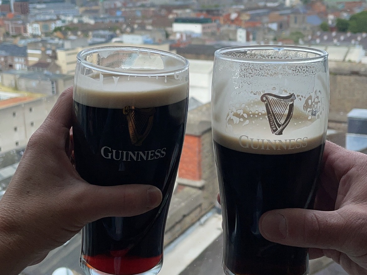 Two people clinking pints of Guinness of beer with a city view in the background.