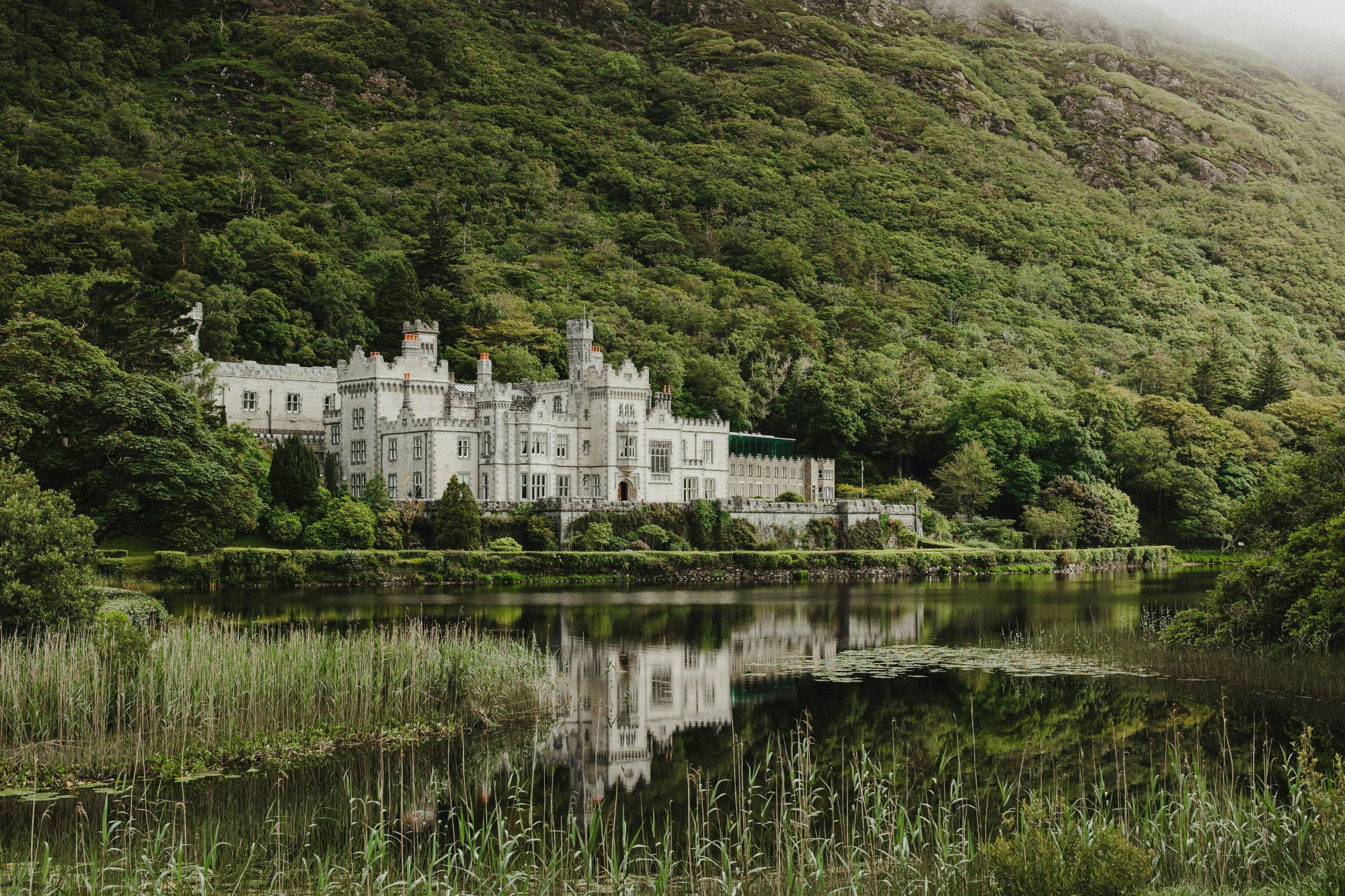 Kylemore Abbey, a large white castle on a lake with green hills surrounding it.