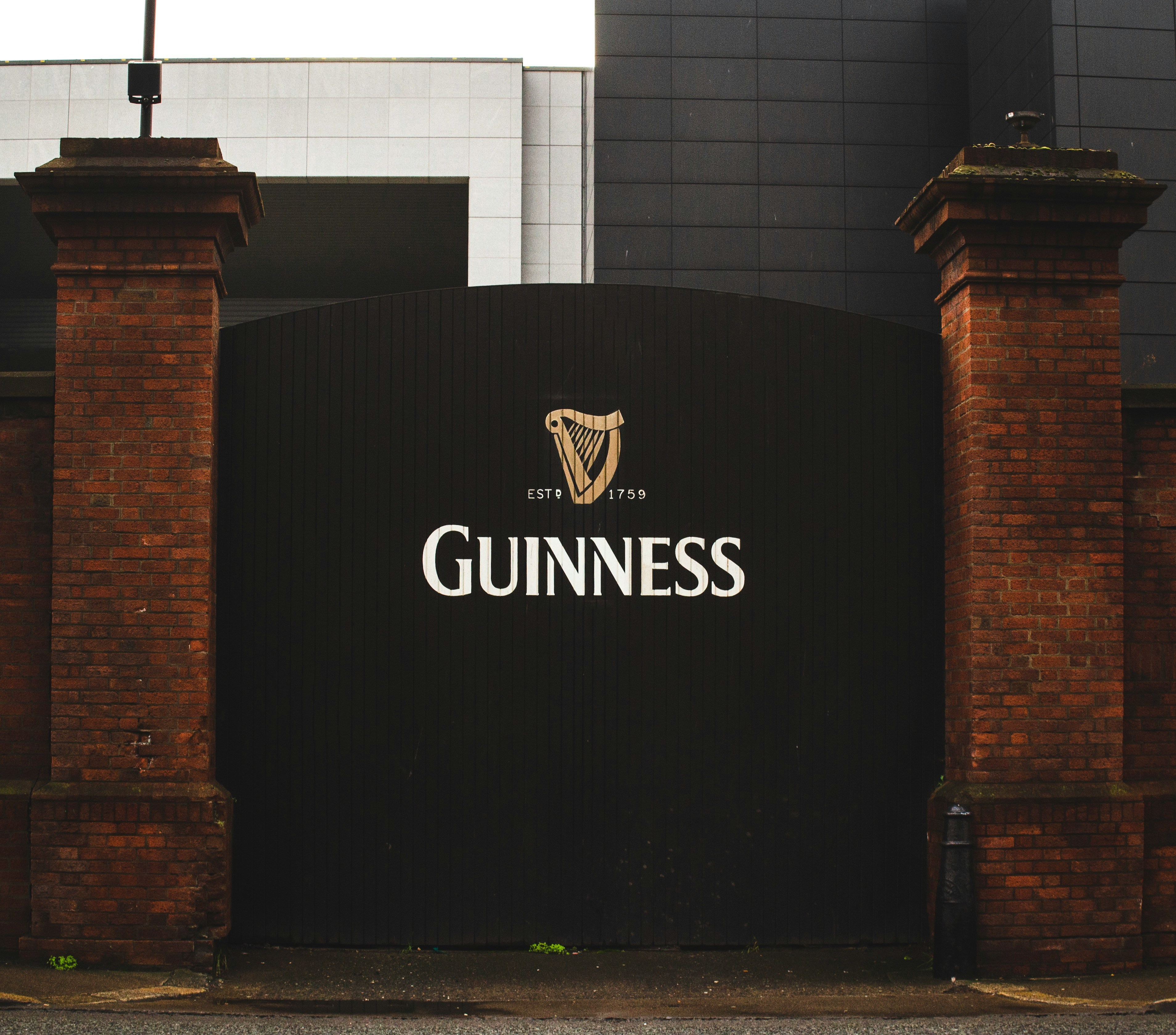 A black gate with the Guinness logo on it and brick columns on either side.