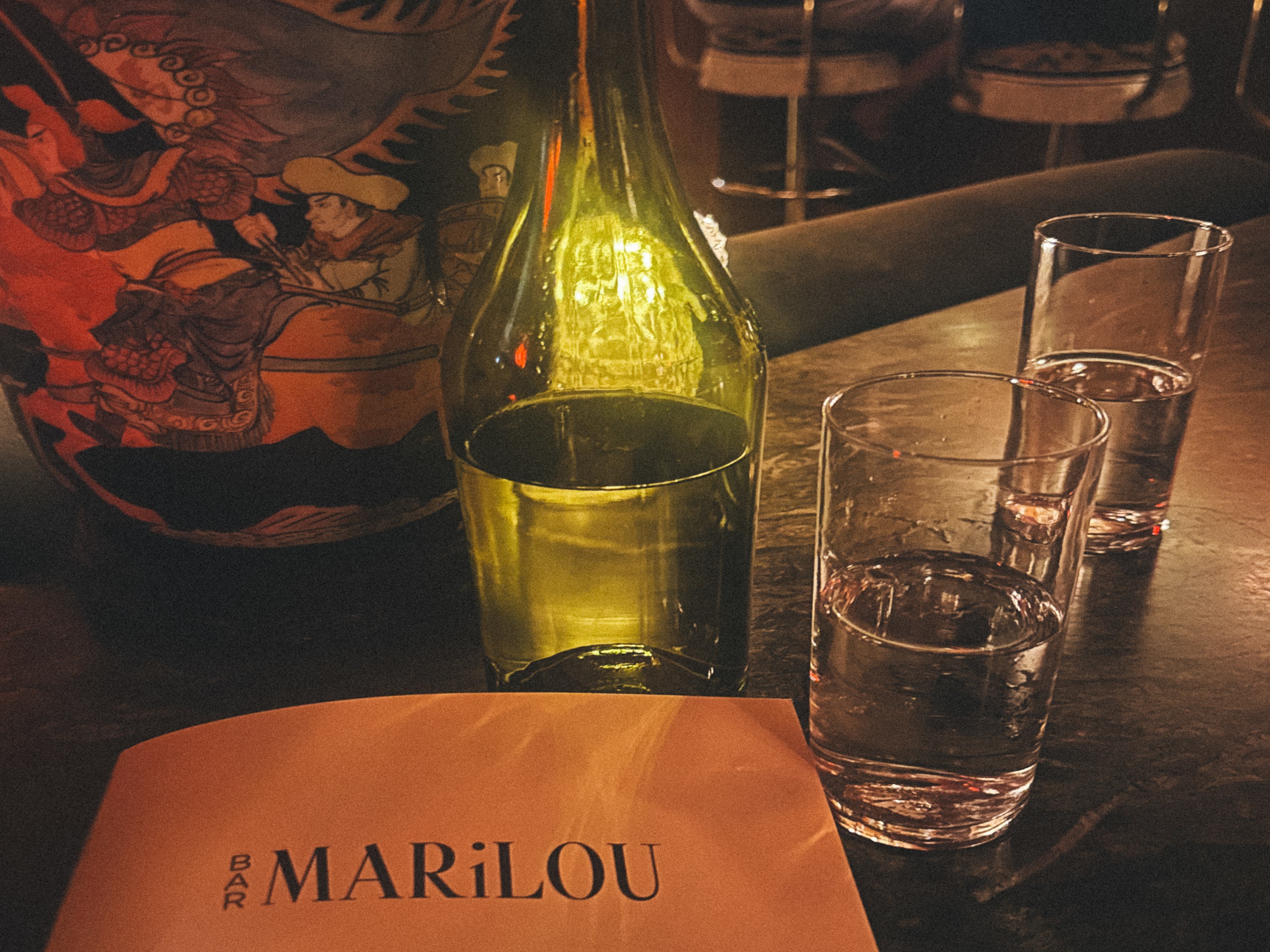 A cozy dining ambiance with a wine bottle, two glasses, and a menu named “MARILOU.”